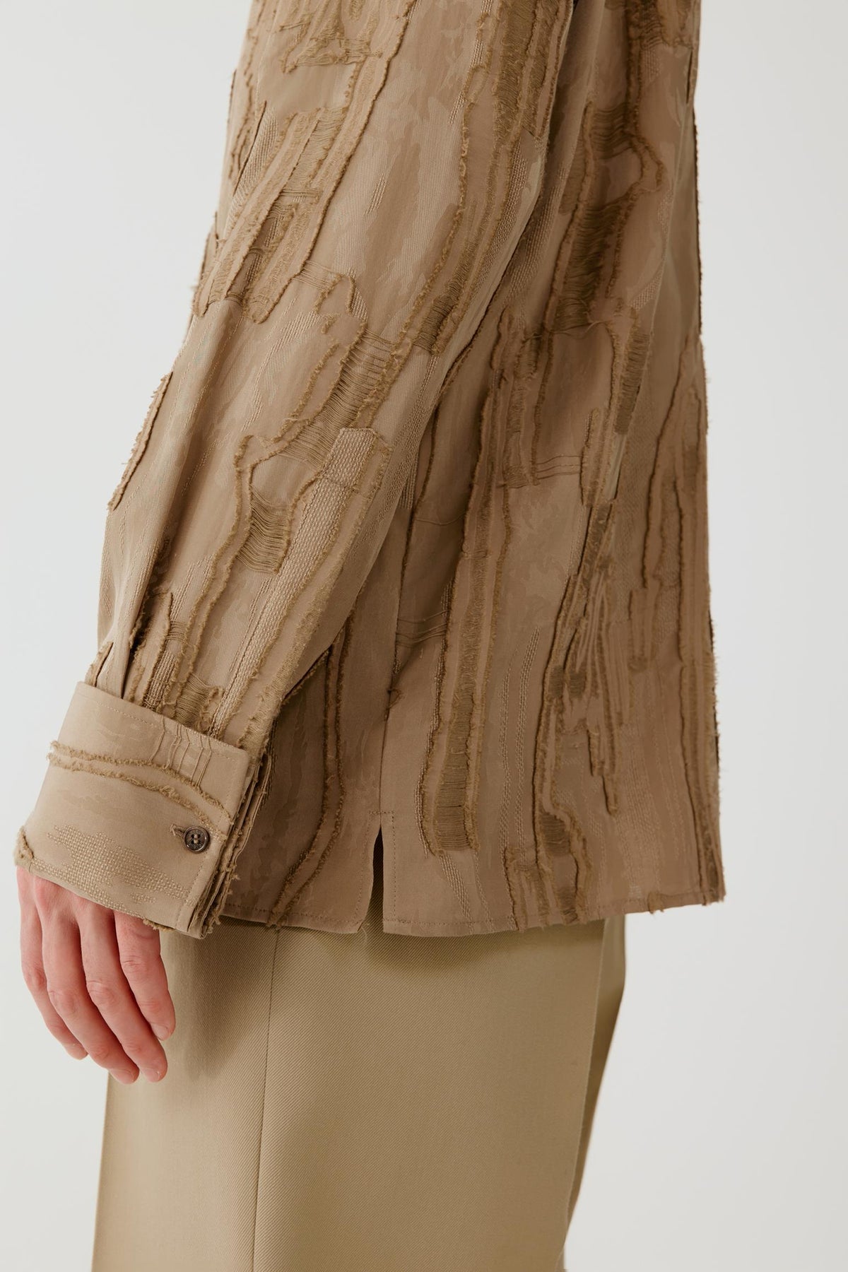 Close-up of the sleeve and adjustable buttoned cuff, showing the textured jacquard surface and camel shade.