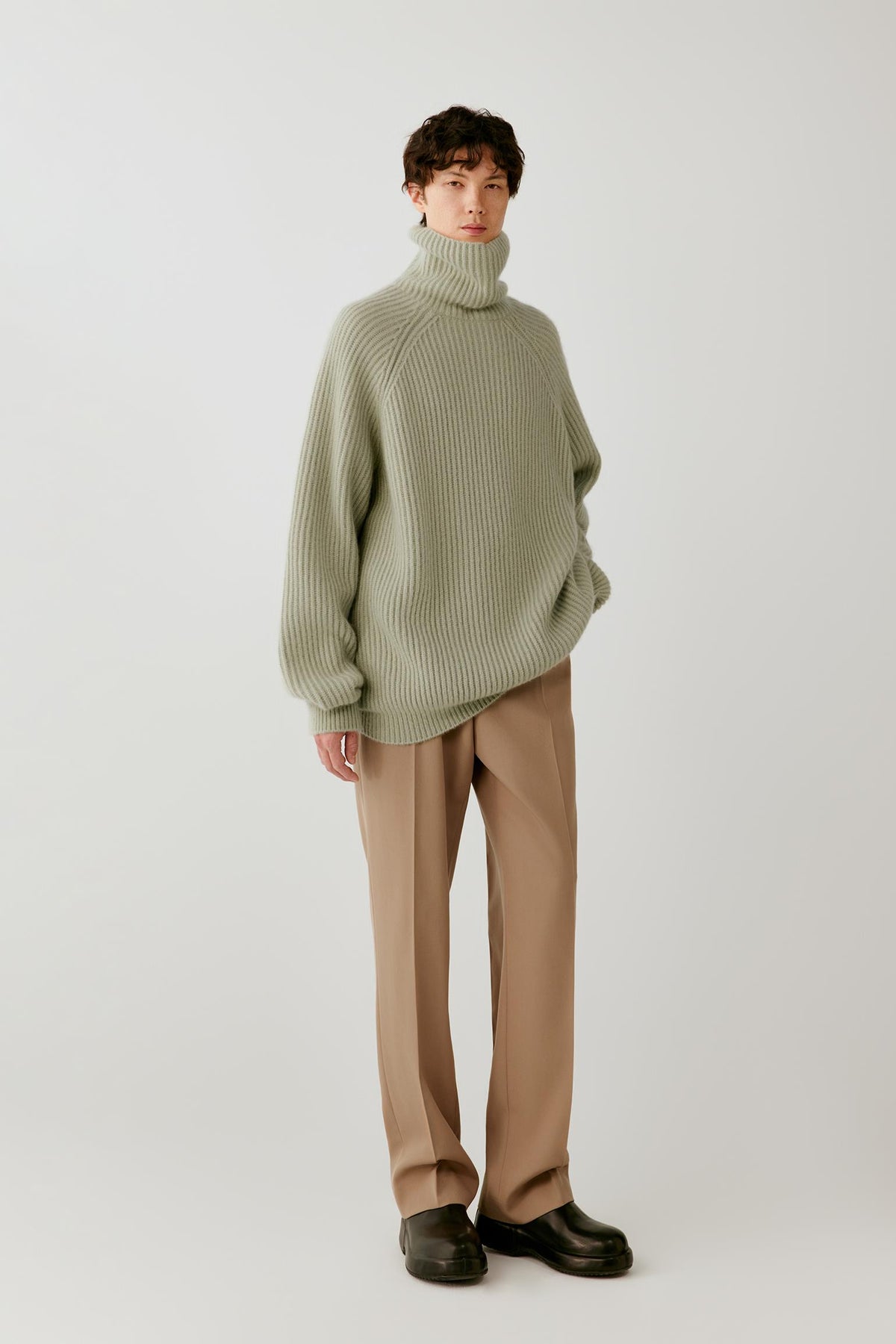 Front view of a man wearing a sage green cashmere and silk pullover, highlighting the oversized silhouette, folded turtleneck and ribbed knit.