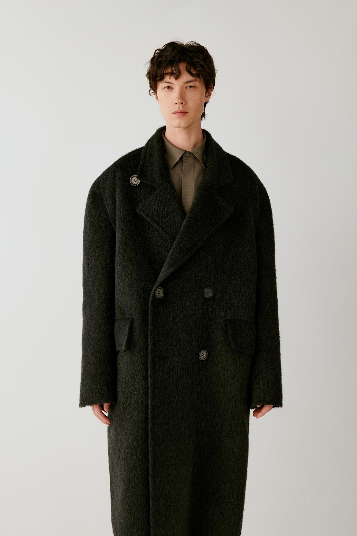 Three-quarter view highlighting the double-breasted front, wide lapels and substantial textured construction of the charcoal grey camel and mohair coat.