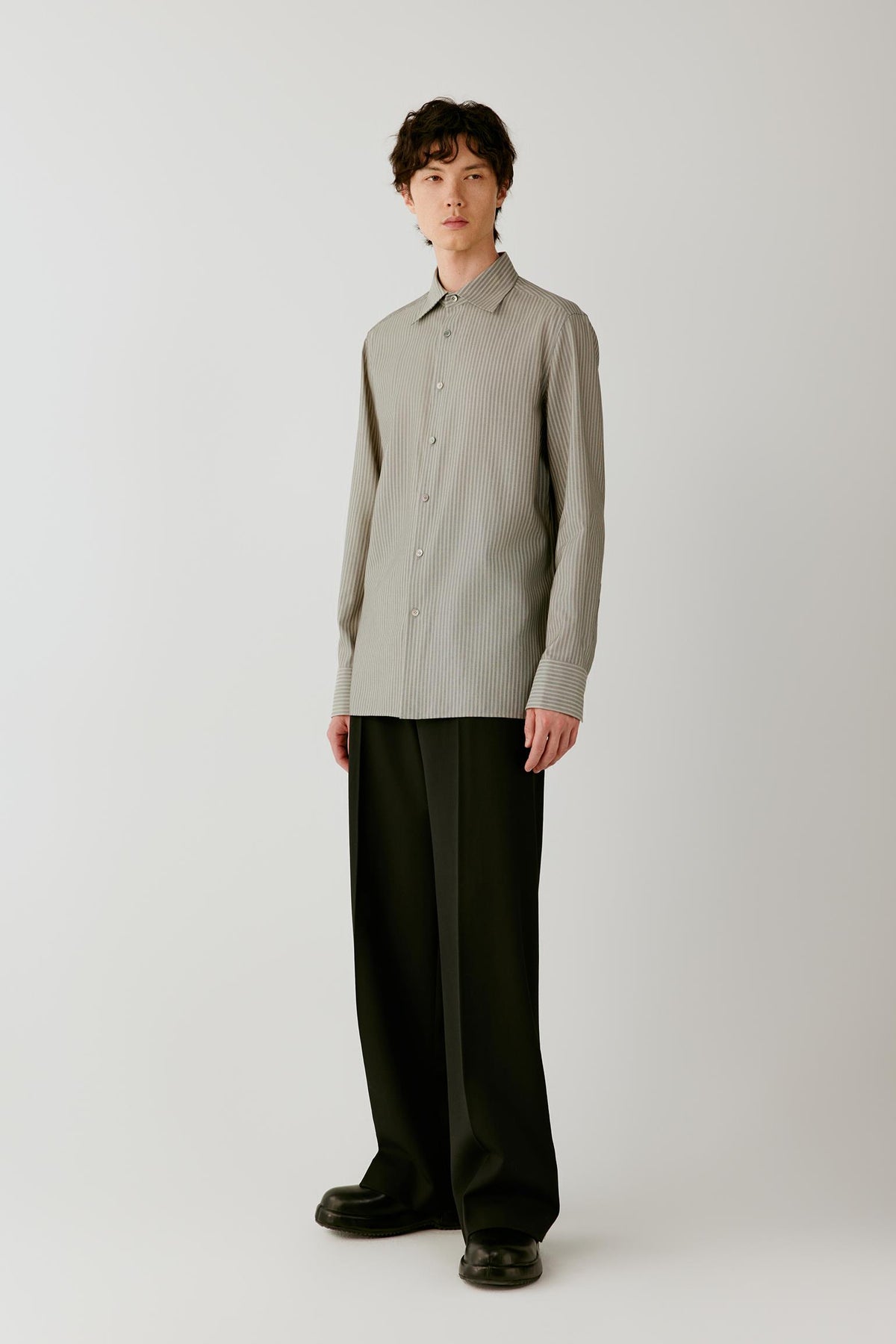Full-length side view showing the long-sleeved striped shirt with black trousers, highlighting its relaxed fit and elongated hem.