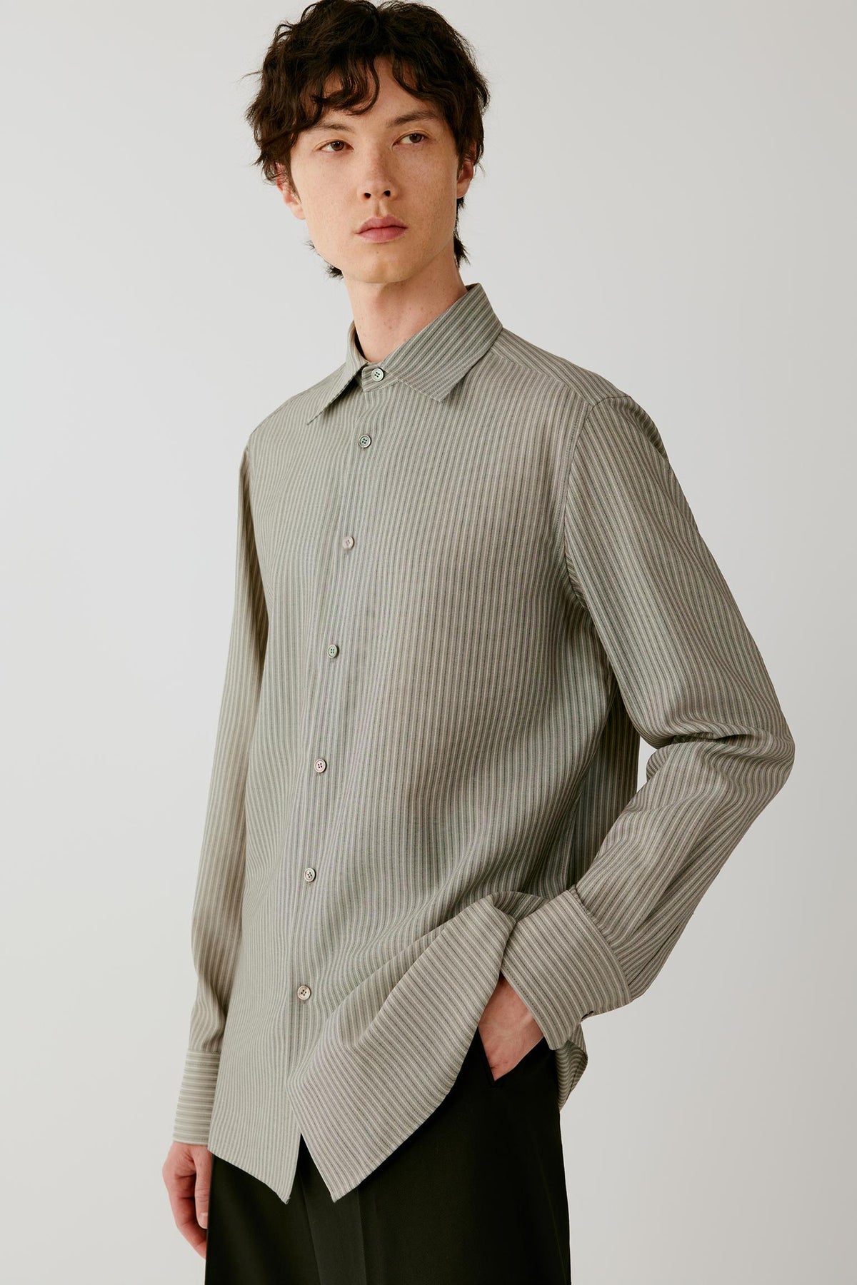 Three-quarter front view of a man wearing a fine grey striped wool and silk shirt, highlighting the relaxed silhouette, pointed collar and vertical stripe pattern.