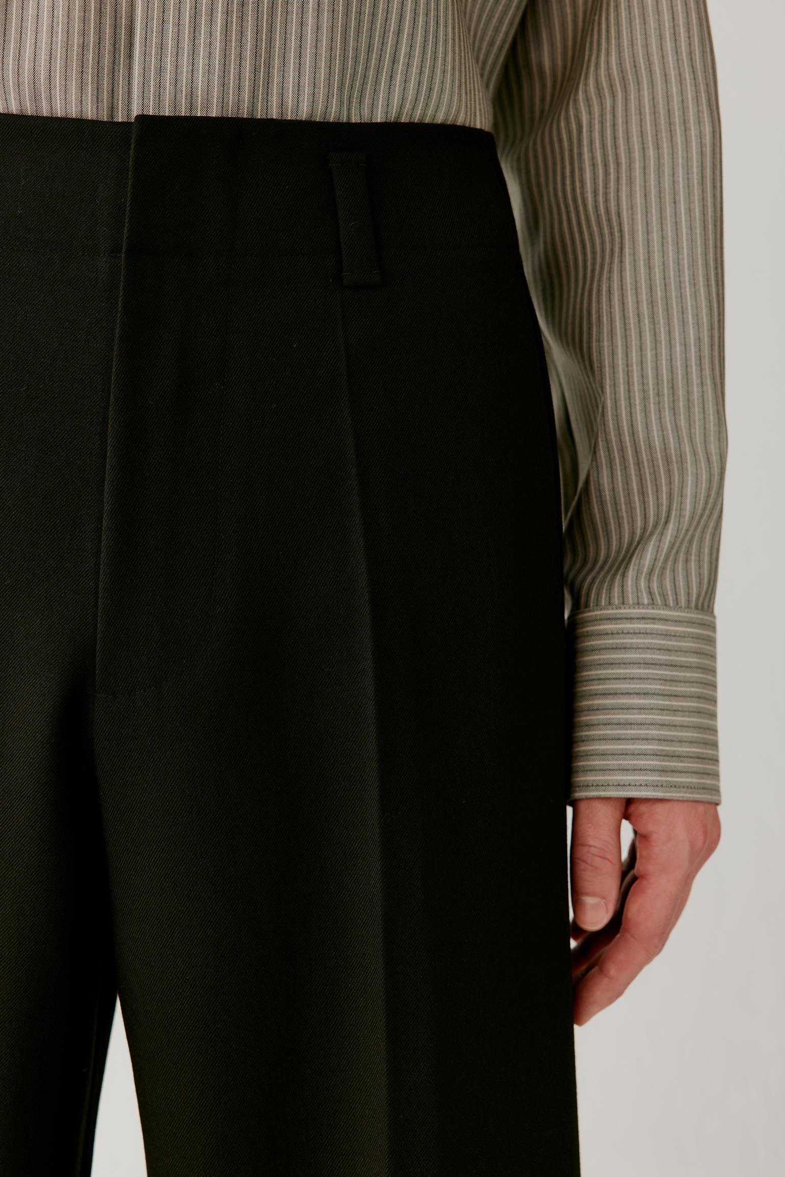 Close-up of the upper trousers showing the double front pleats, waistband and smooth, structured surface.
