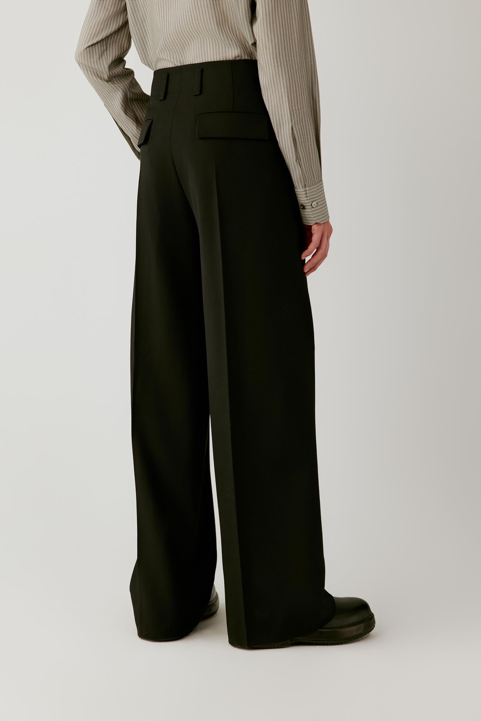 Three-quarter view highlighting the wide-leg silhouette, front pleats and clean fall of the black wool twill.