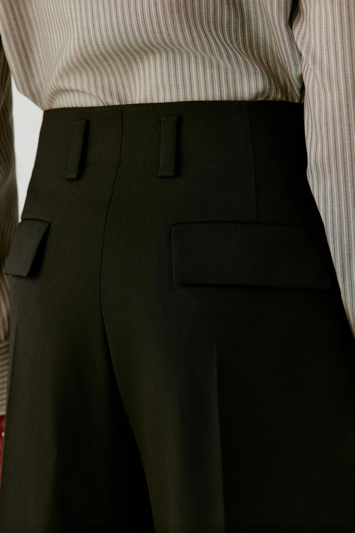 Close-up highlighting the waistband, belt loops and front pleat construction of the deep black wool twill trousers.