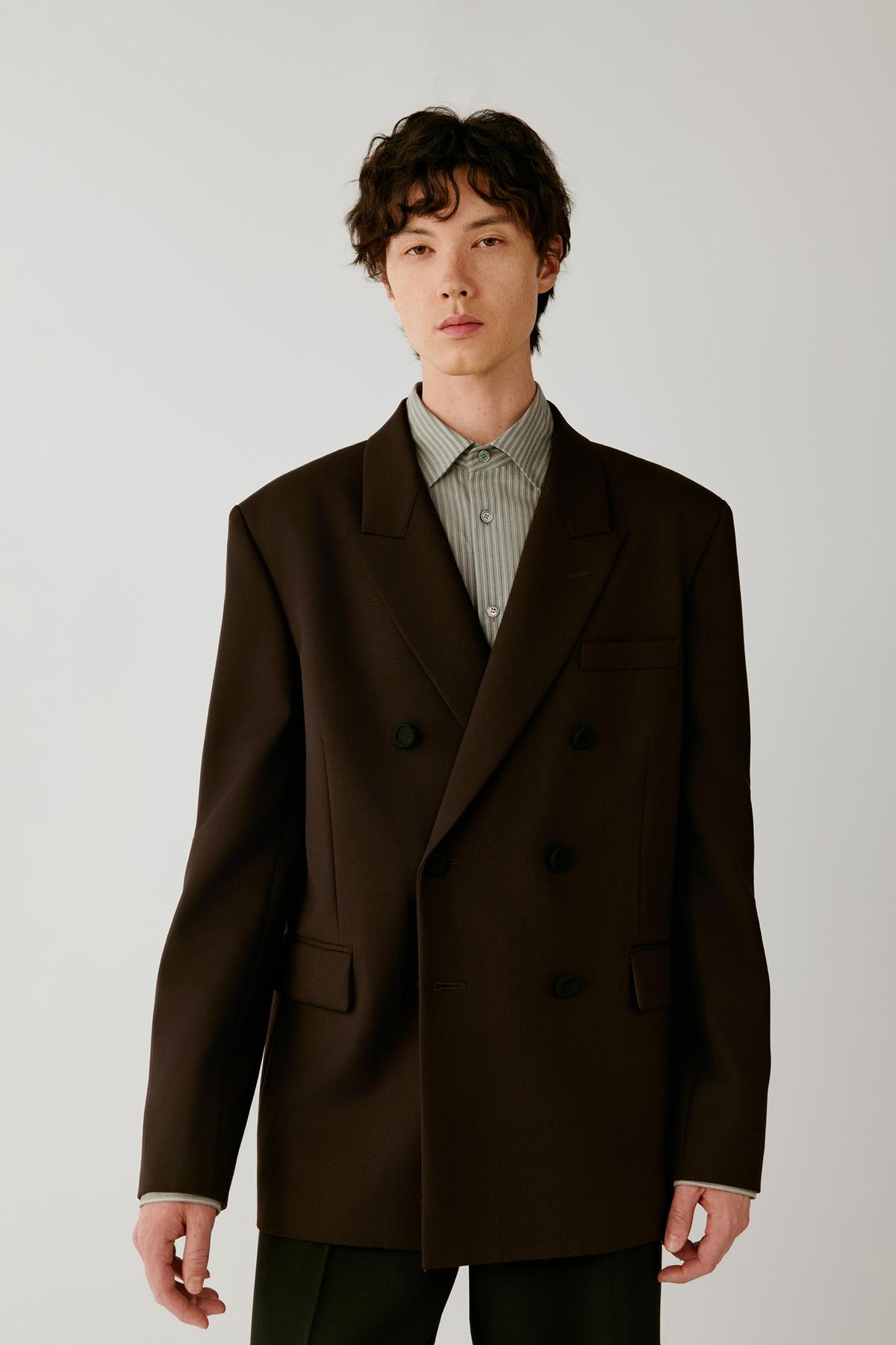 Front view of a man wearing a deep black wool twill jacket, highlighting the double-breasted silhouette, broad peak lapels and elongated cut.