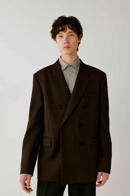 Front view of a man wearing a deep black wool twill jacket, highlighting the double-breasted silhouette, broad peak lapels and elongated cut.