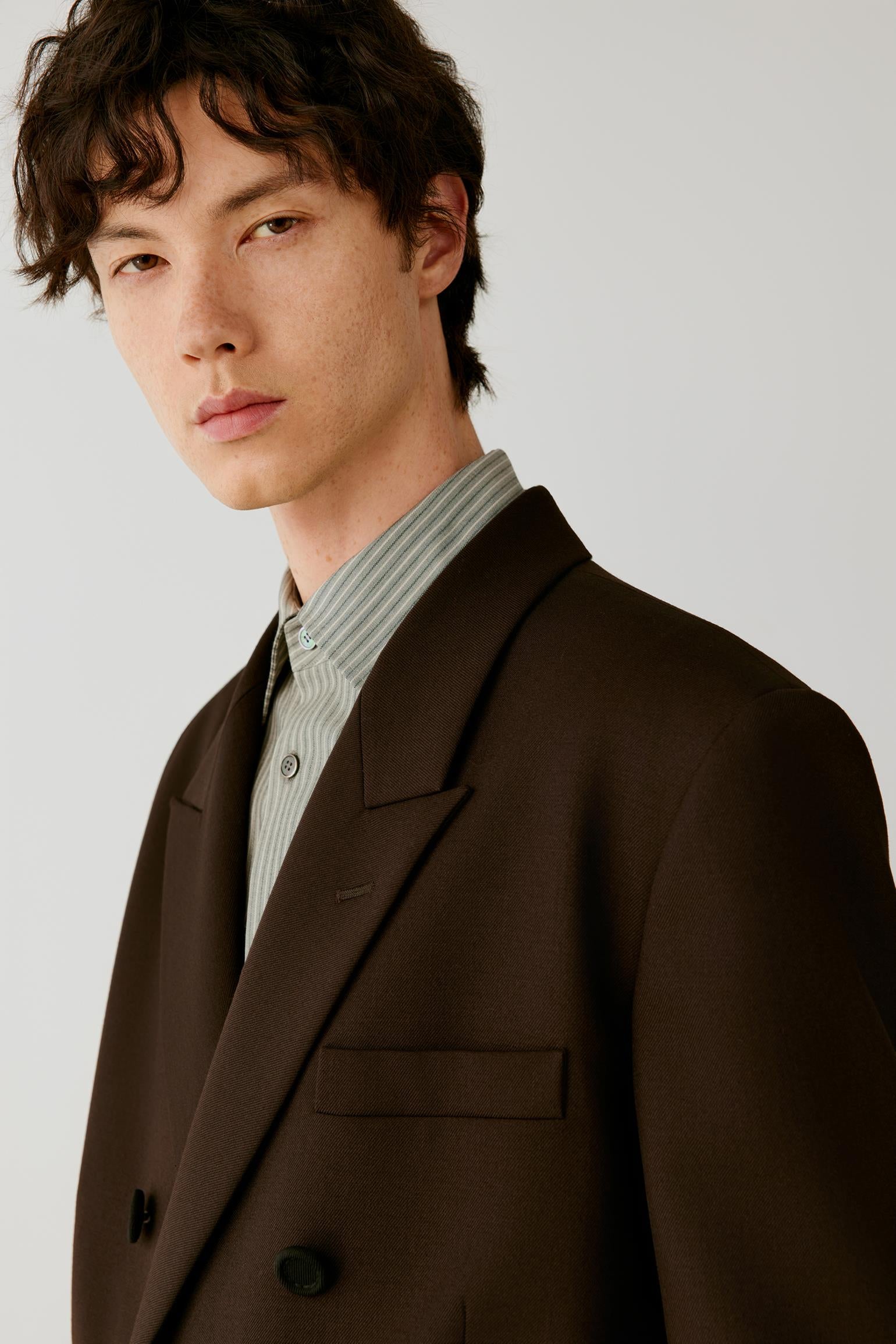 Close-up highlighting the broad peak lapels, double-breasted fastening and smooth, compact surface of the wool twill.