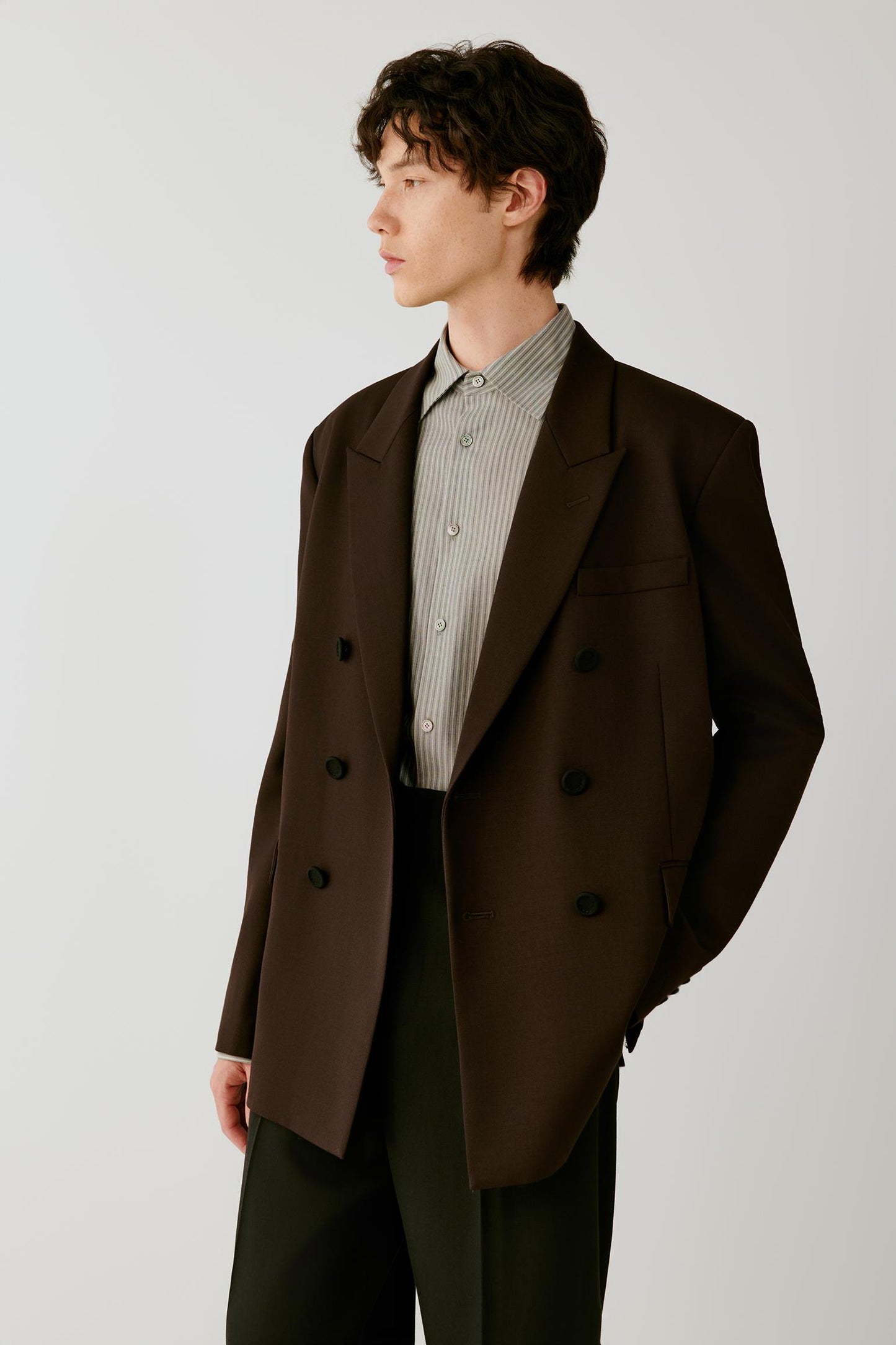 Three-quarter front view emphasizing the peak lapels, double-breasted construction and structured wool twill fabric.