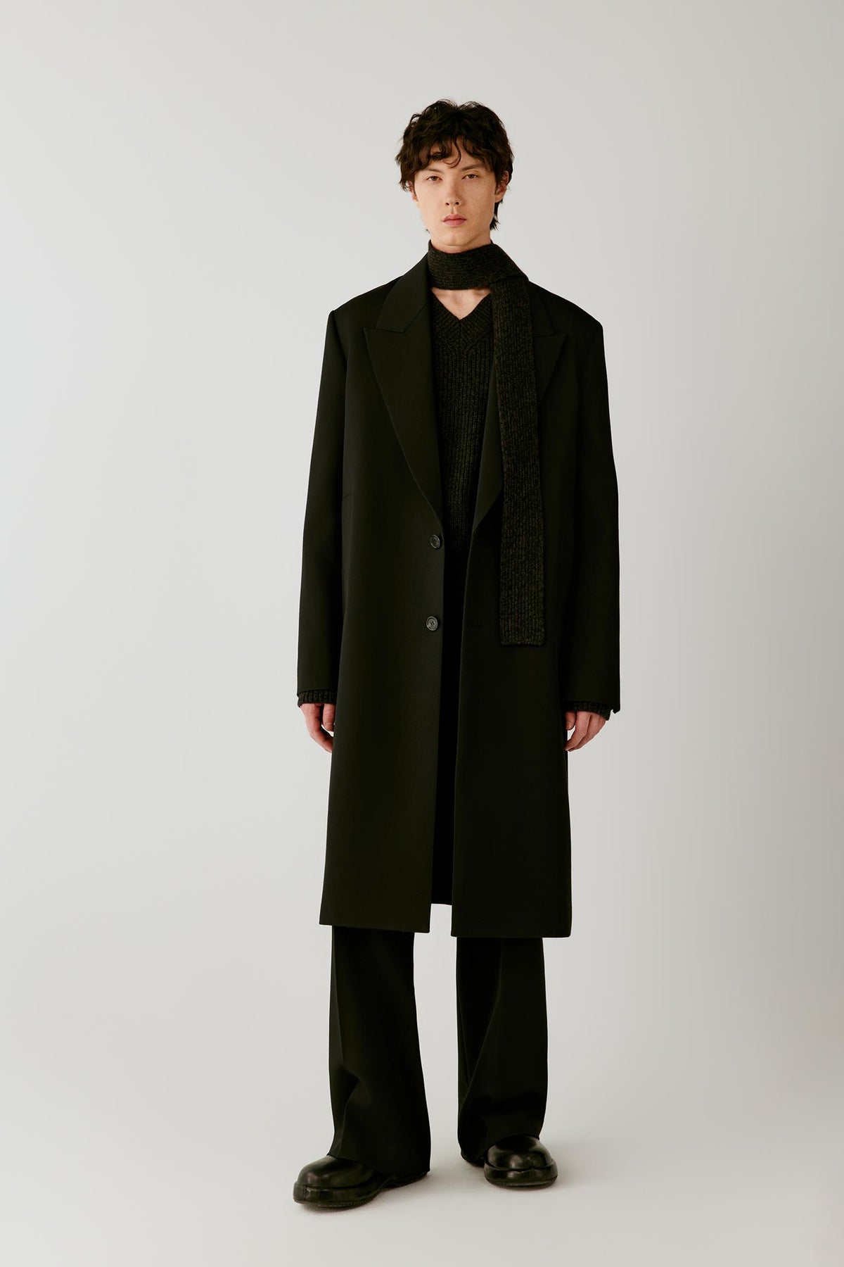Front view of a man wearing a deep black double-face wool coat, showing the long straight silhouette, pronounced peak lapels and single-breasted front.