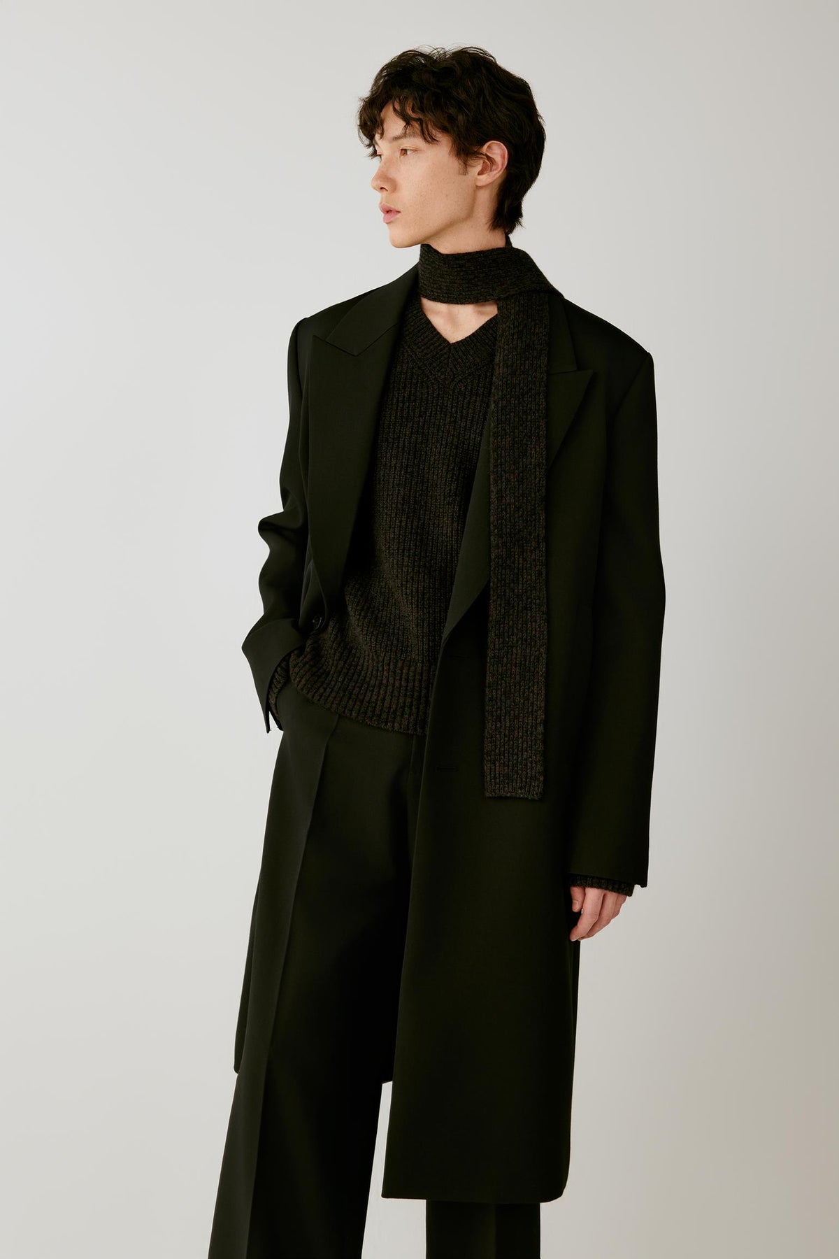 Three-quarter view highlighting the elongated cut, peak lapels and structured drape of the deep black double-face wool coat.