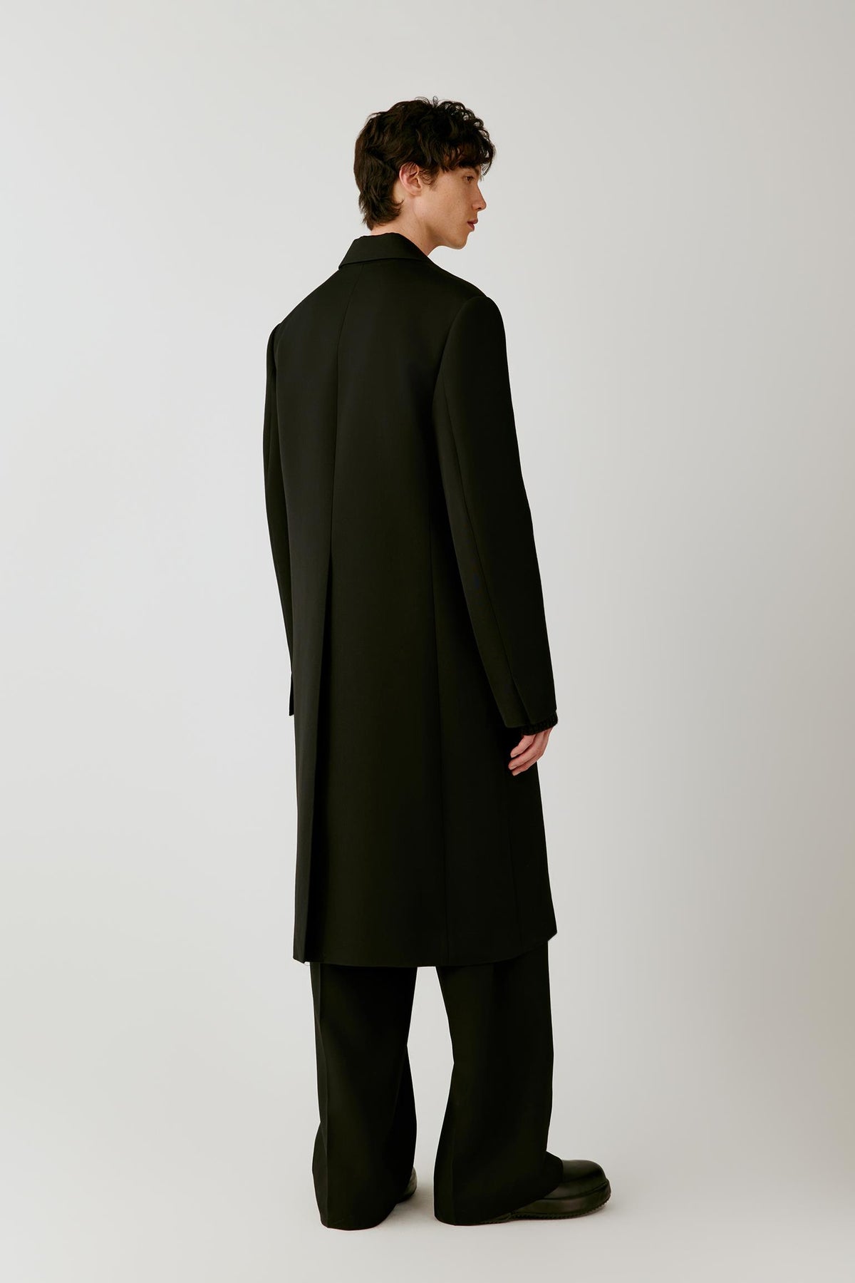 Back view of a man wearing the deep black double-face wool coat, showing the long straight silhouette and clean tailored construction.