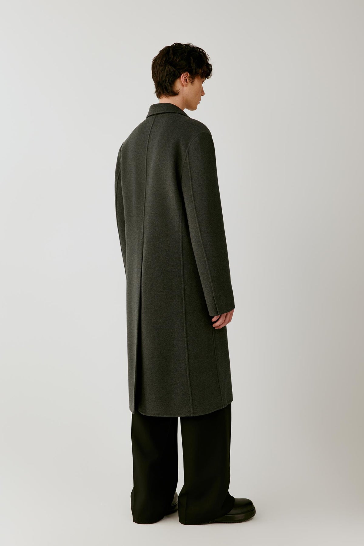 Back view of a man wearing a dark grey melange double-face wool coat, showing the elongated silhouette and clean construction.
