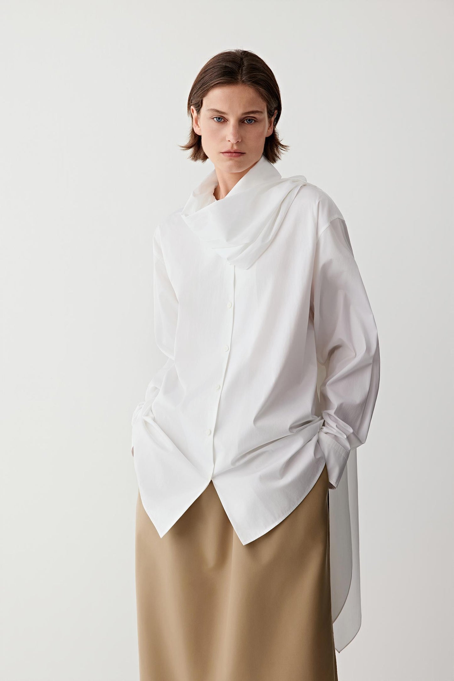 Woman wearing a white cotton poplin shirt with beige trousers, three-quarter view.