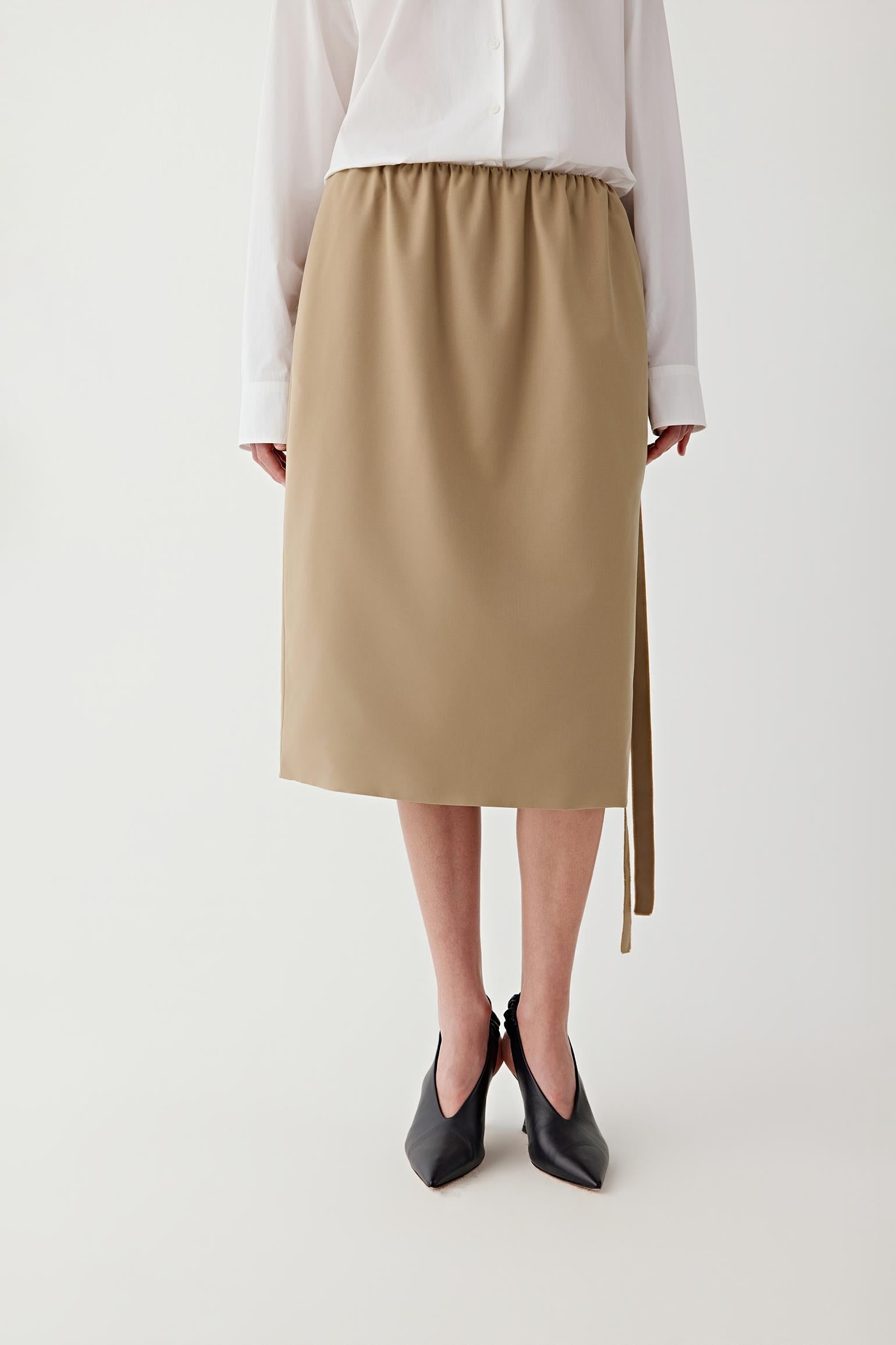 Woman wearing a beige skirt with a white shirt on a plain background