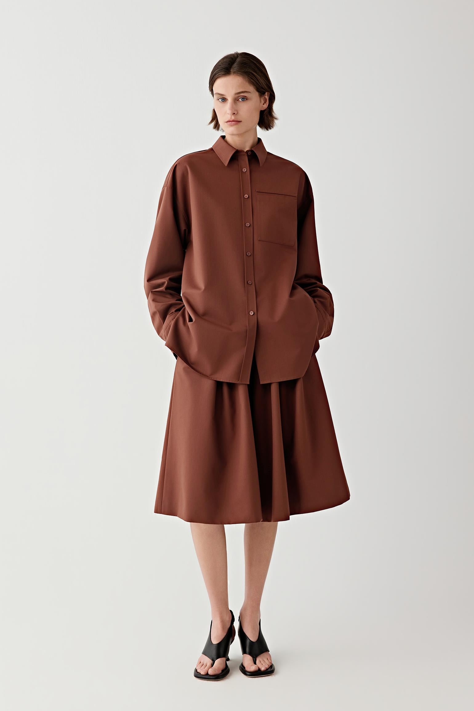 Woman wearing a brown shirt and brown skirt with a white background