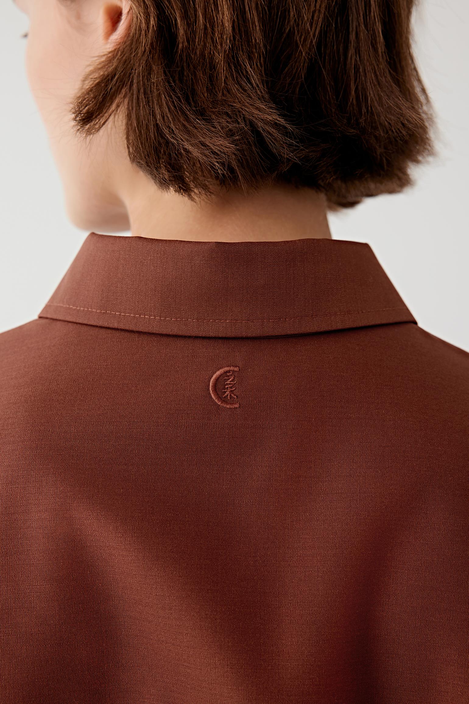Brown shirt with a small embroidered design on the collar against a white background