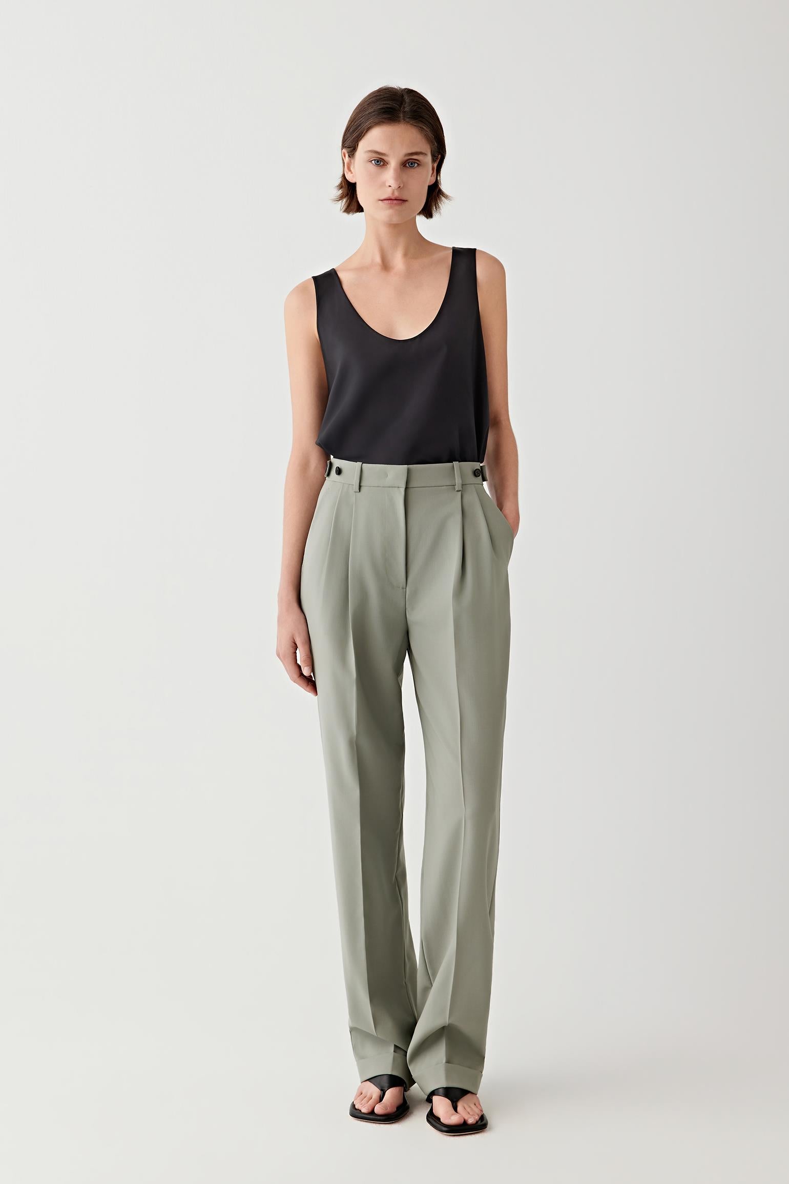 Woman wearing a black sleeveless top and green high-waisted pants on a white background