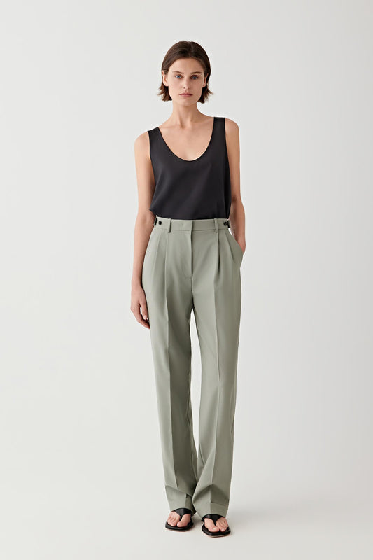 Woman wearing a black sleeveless top and green high-waisted pants on a white background