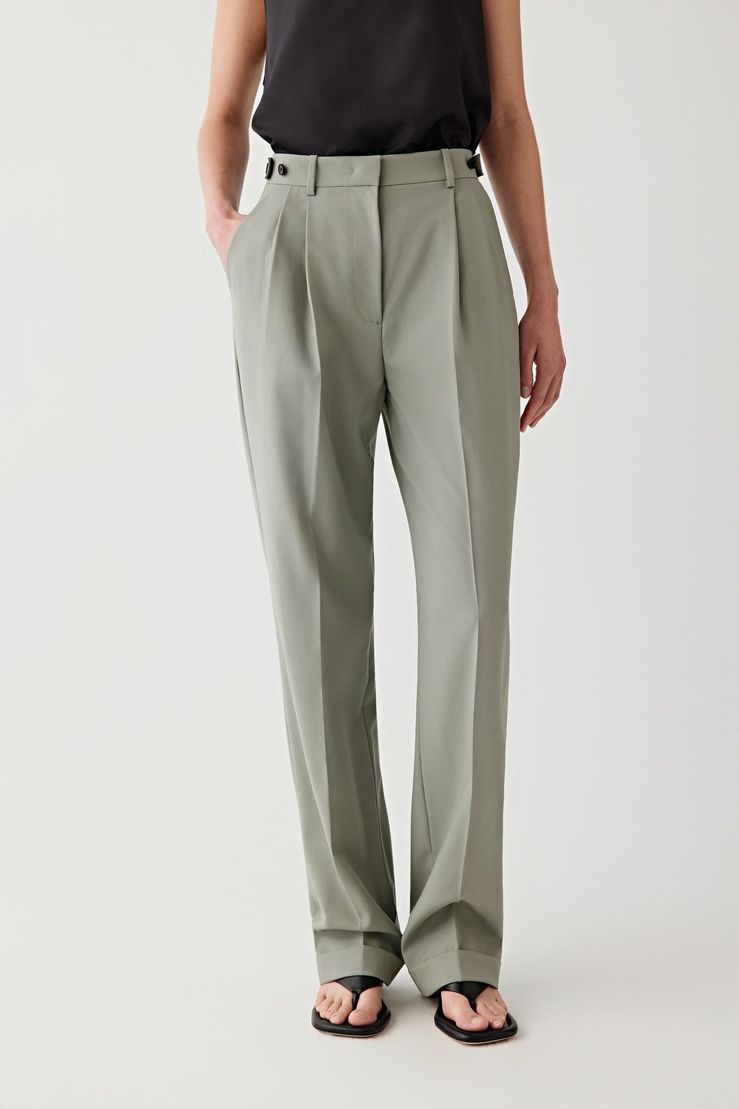 Person wearing light gray pleated pants on a white background