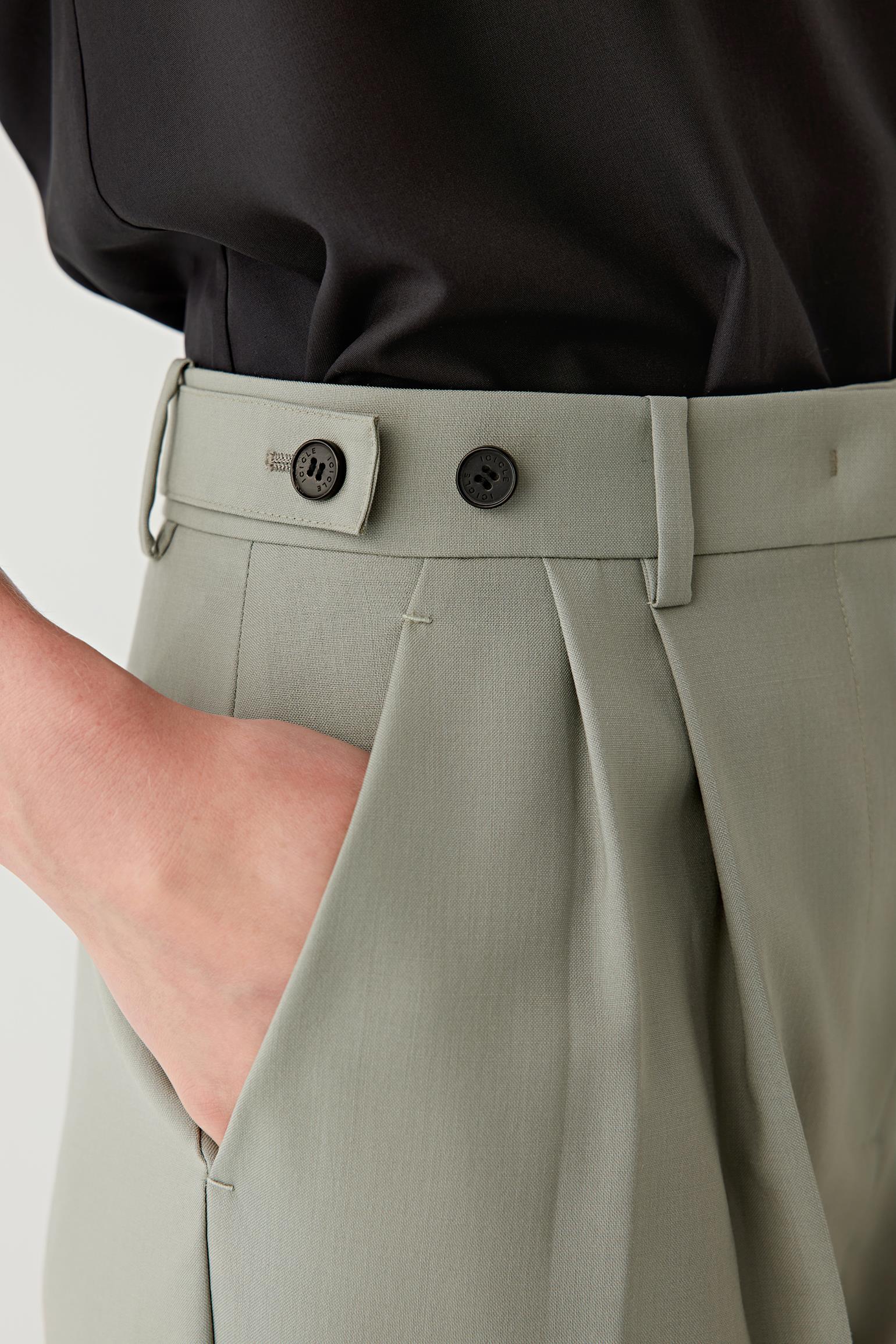 Person wearing light gray pleated pants with a black shirt on a white background