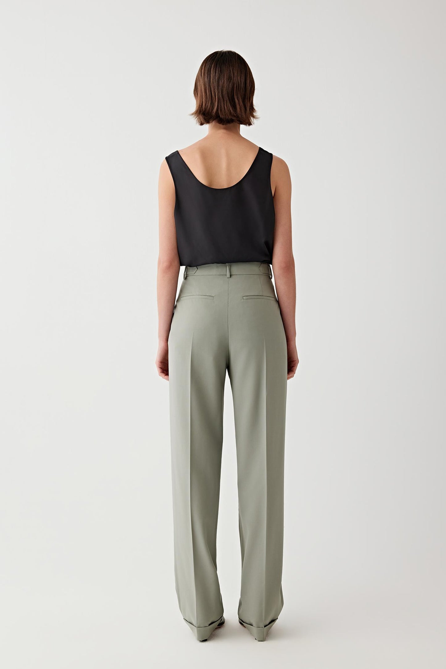 Person wearing a black sleeveless top and light green pants on a white background