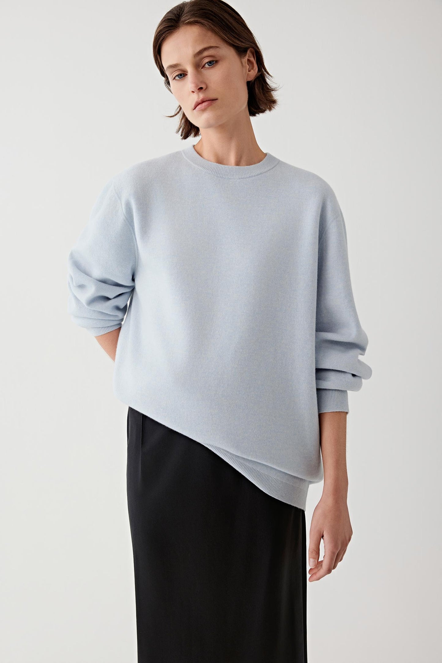 Woman wearing a light blue wool and cashmere pullover with black trousers, three-quarter view.
