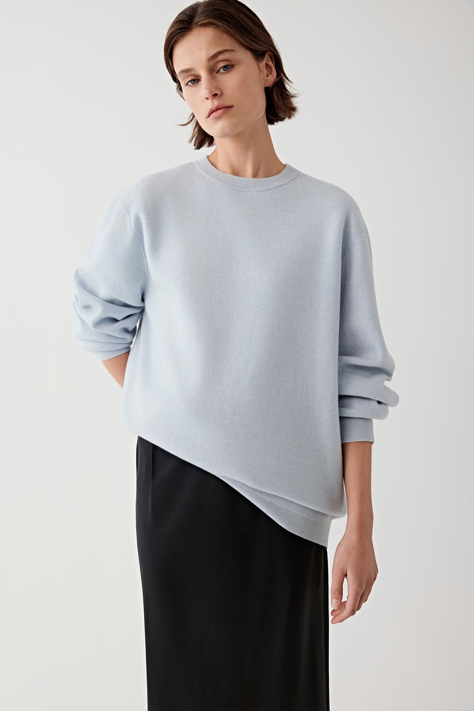 Woman wearing a light blue wool and cashmere pullover with black trousers, three-quarter view.