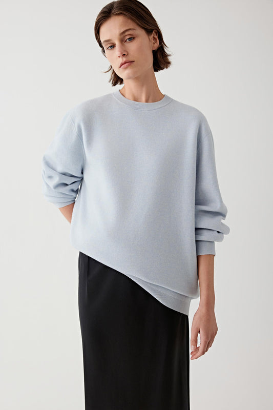 Woman wearing a light blue wool and cashmere pullover with black trousers, three-quarter view.