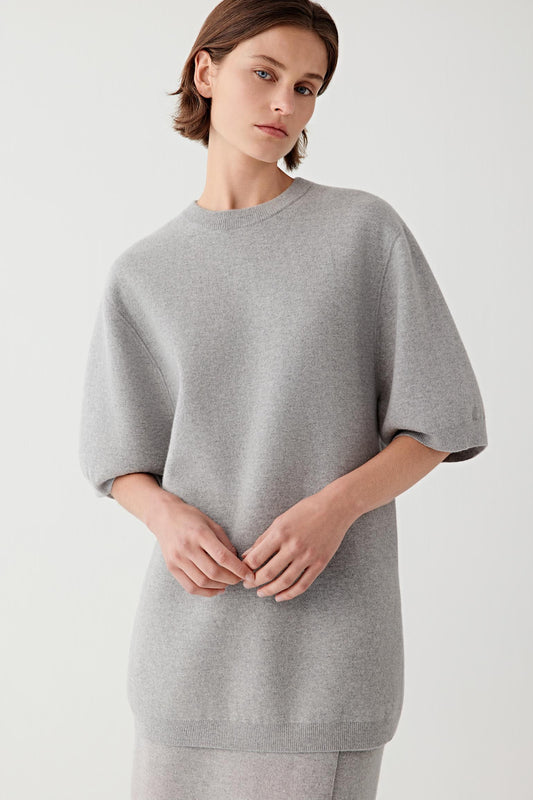 Woman wearing a light grey short-sleeve wool and cashmere pullover, three-quarter view.