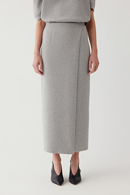 Woman wearing a long light grey wool and cashmere skirt with a matching short-sleeve knit, front view.