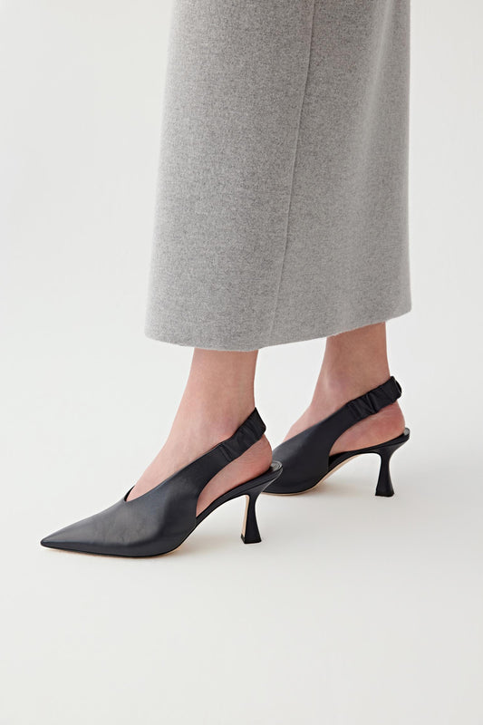 Side view of both feet showing the shoes worn in a natural standing position, emphasizing the curved mid heel, the wide upper and the slingback strap with gathered detail at the back of the heel, as well as the balanced proportion between heel height and sole