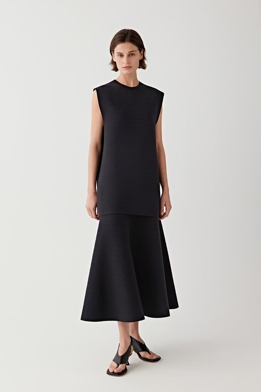 Woman wearing a black sleeveless top with black skirt against a plain background