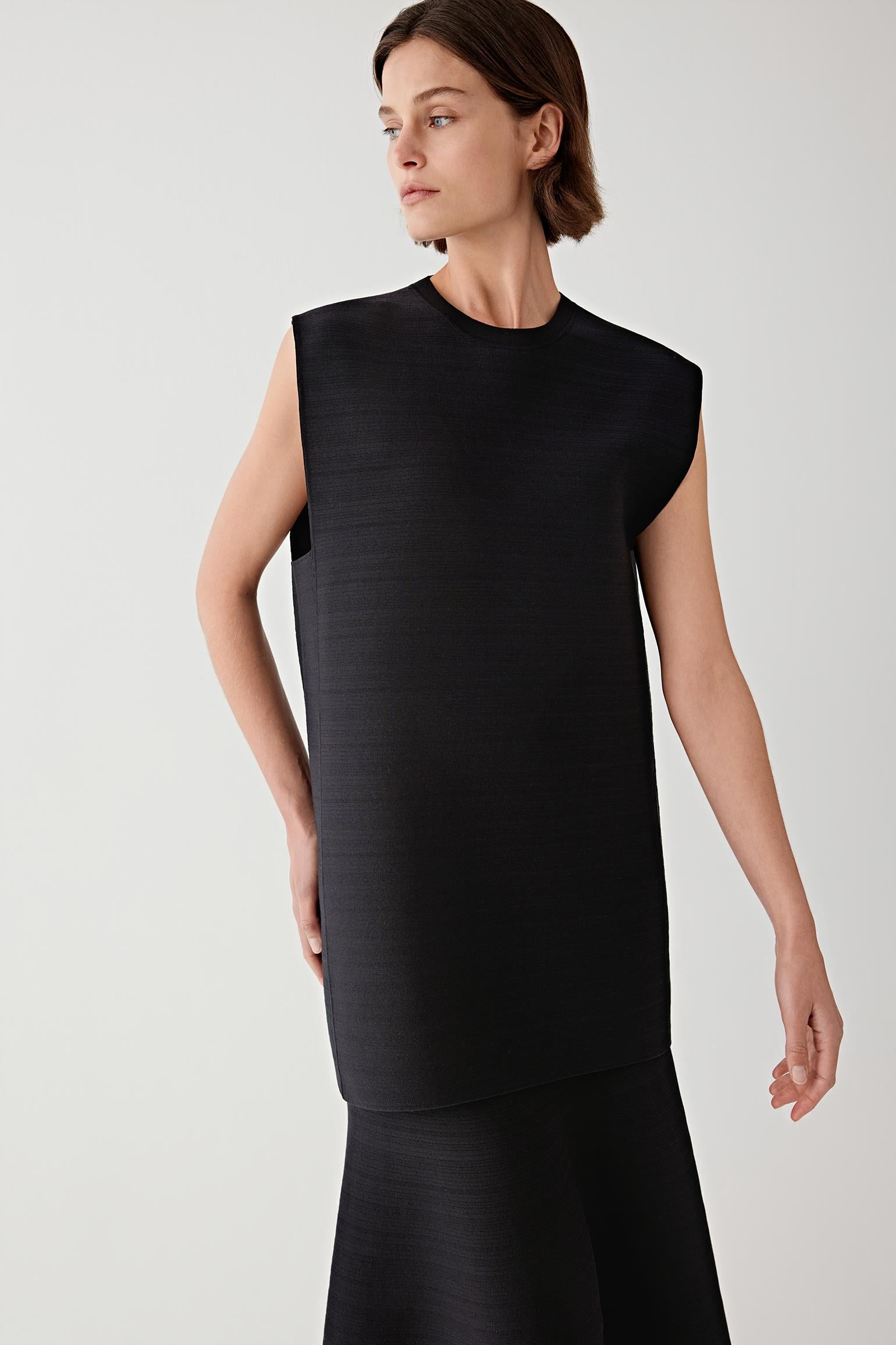 Woman wearing a black sleeveless top with black skirt against a plain background