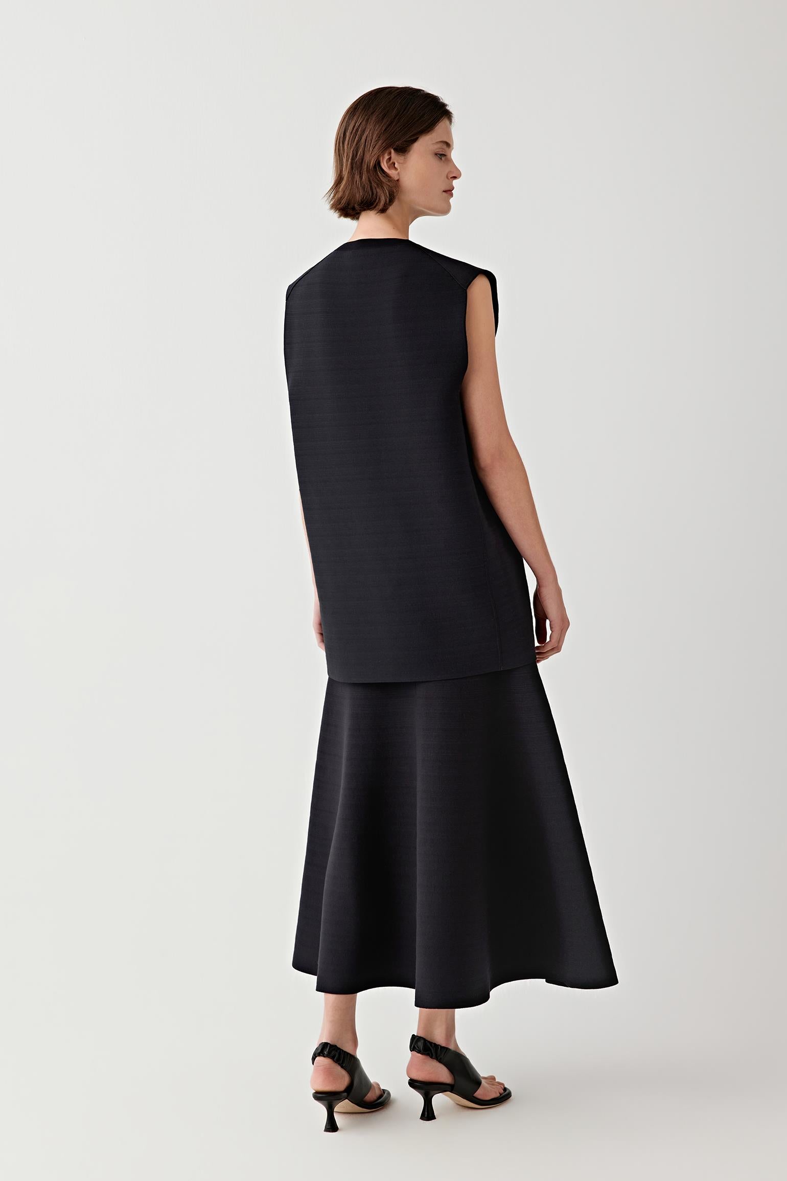 Woman wearing a black sleeveless top with black skirt against a plain background