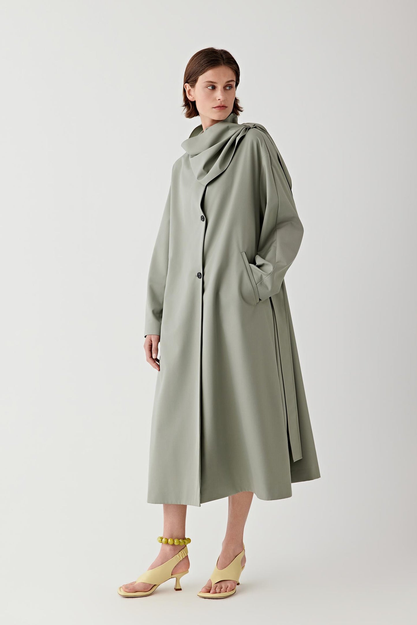 Woman wearing a long green coat on a white background