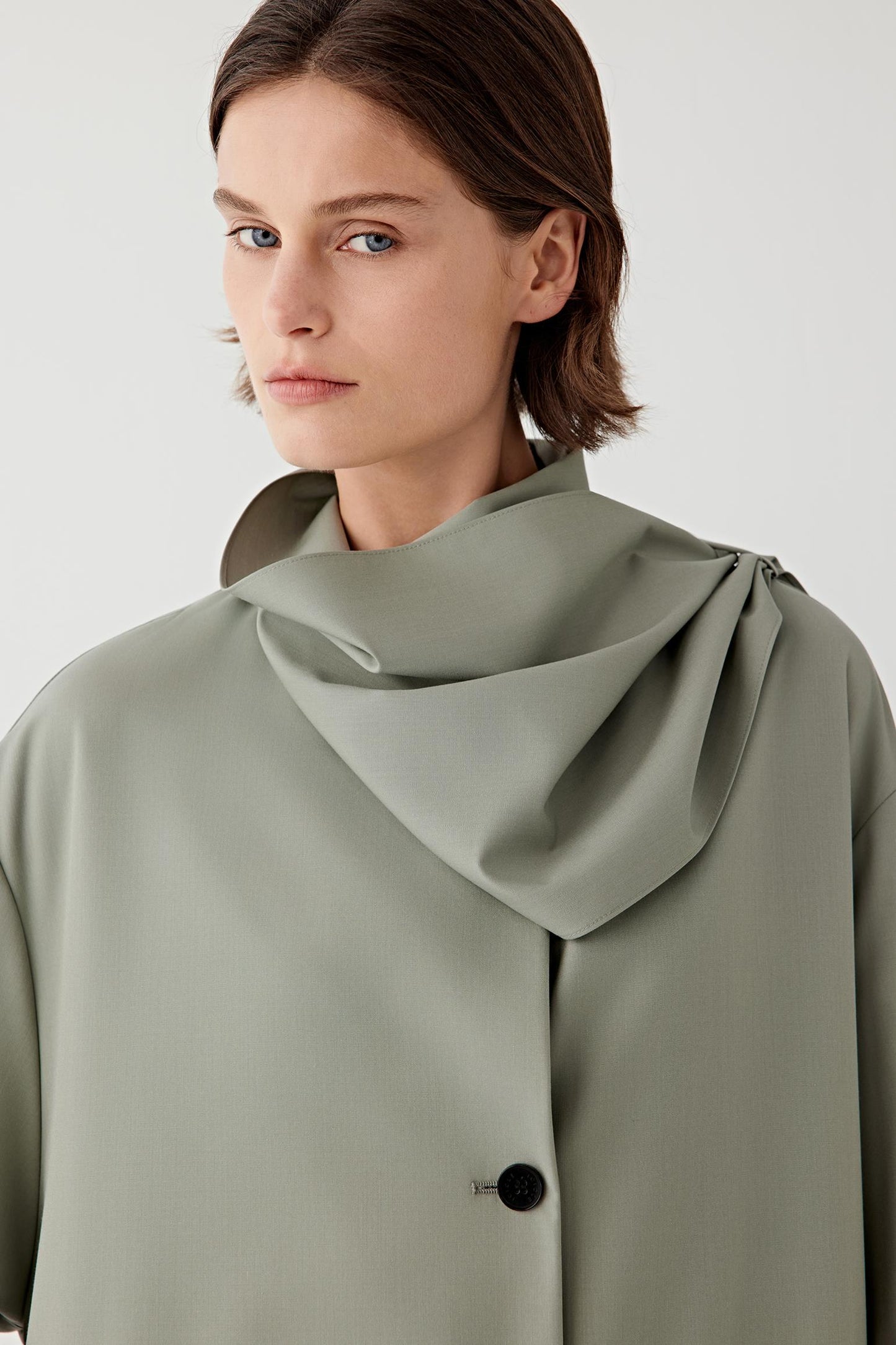 Woman wearing a light green coat with a large collar against a white background