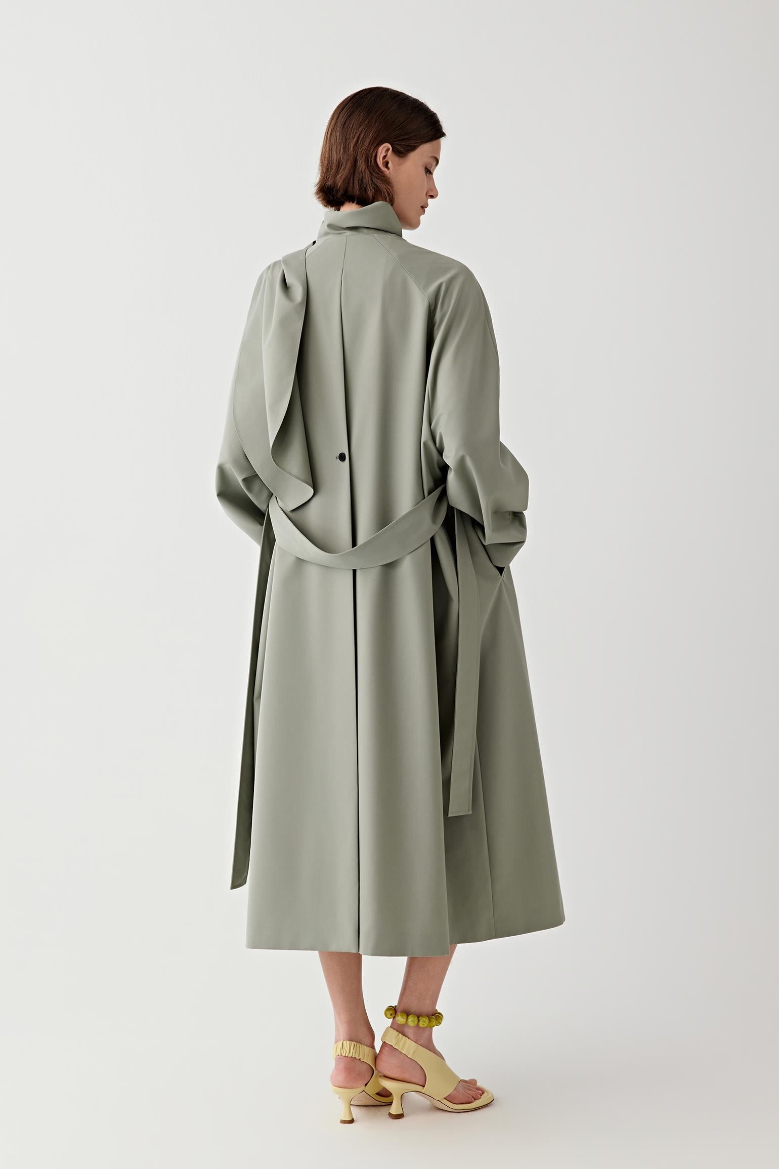 Woman wearing a long green coat on a white background