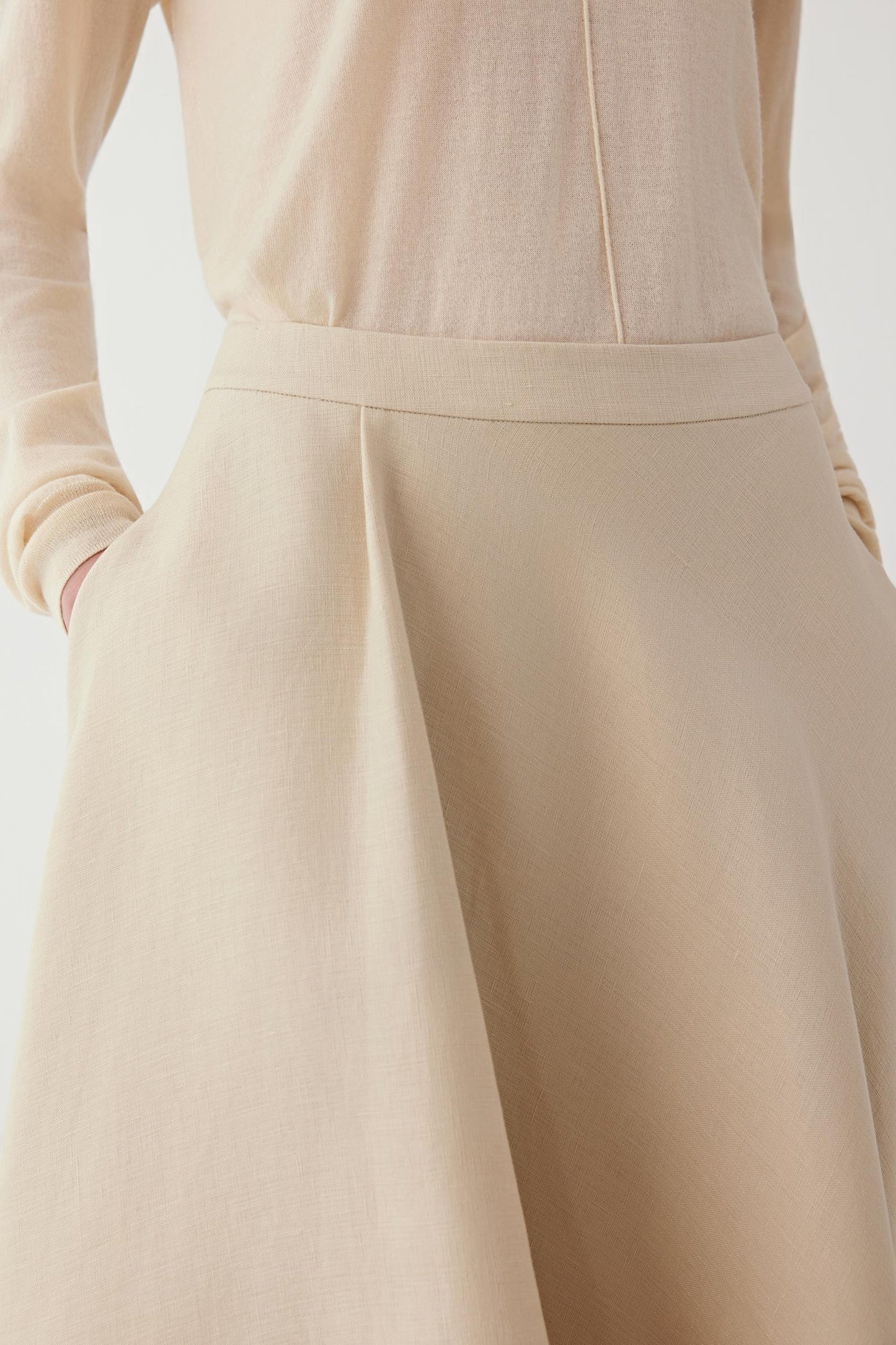 Close-up of the waist of a beige knit maxi skirt with an integrated waistband, structured pleat and textured fabric.