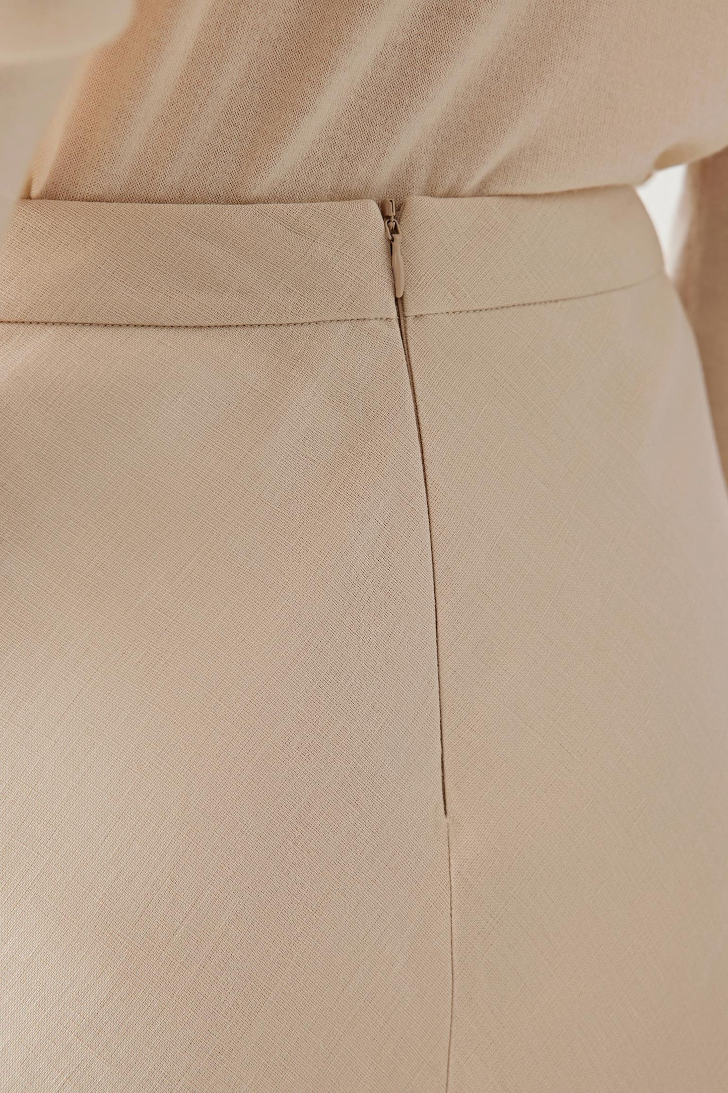 Close-up of the back waist of a beige maxi skirt featuring a concealed zipper closure and clean seam detail.