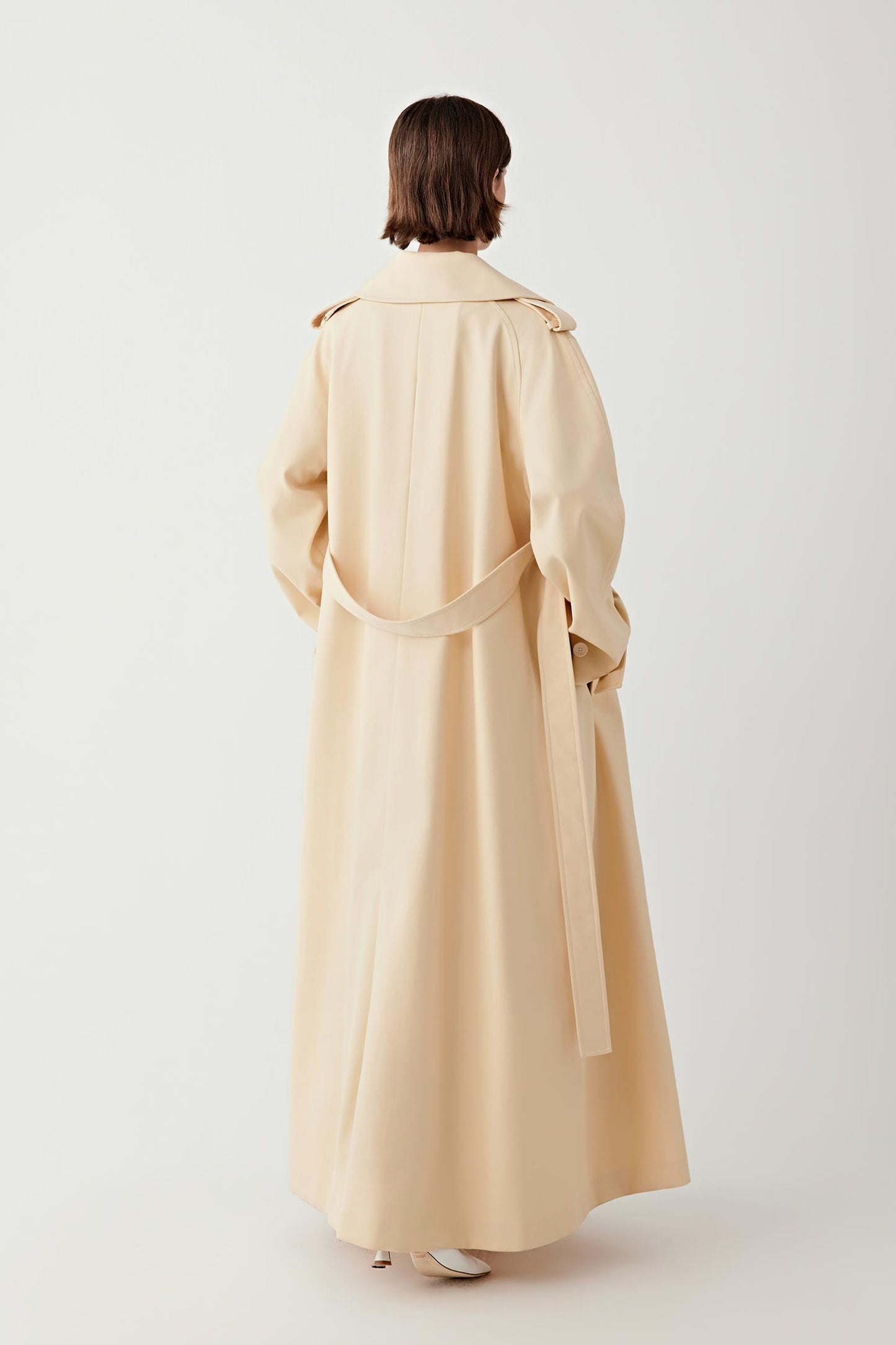 Person wearing a beige trench coat on a white background