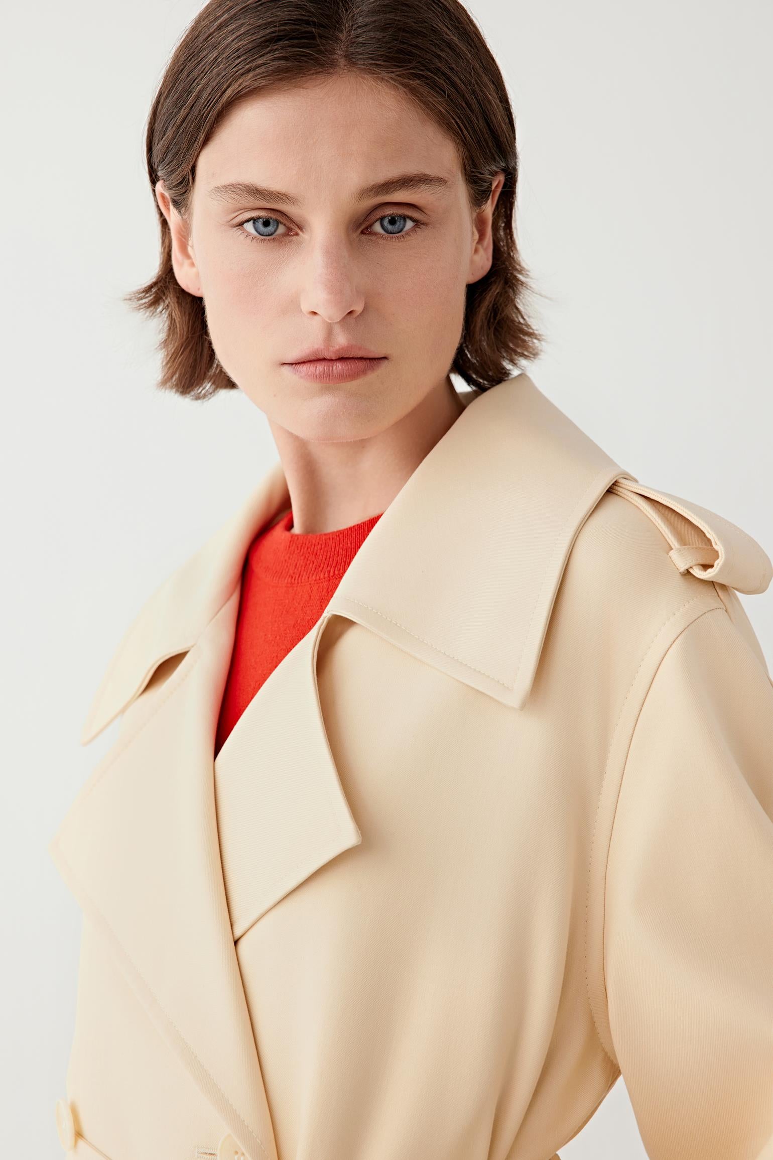 Woman wearing a beige trench coat over a red top on a light background