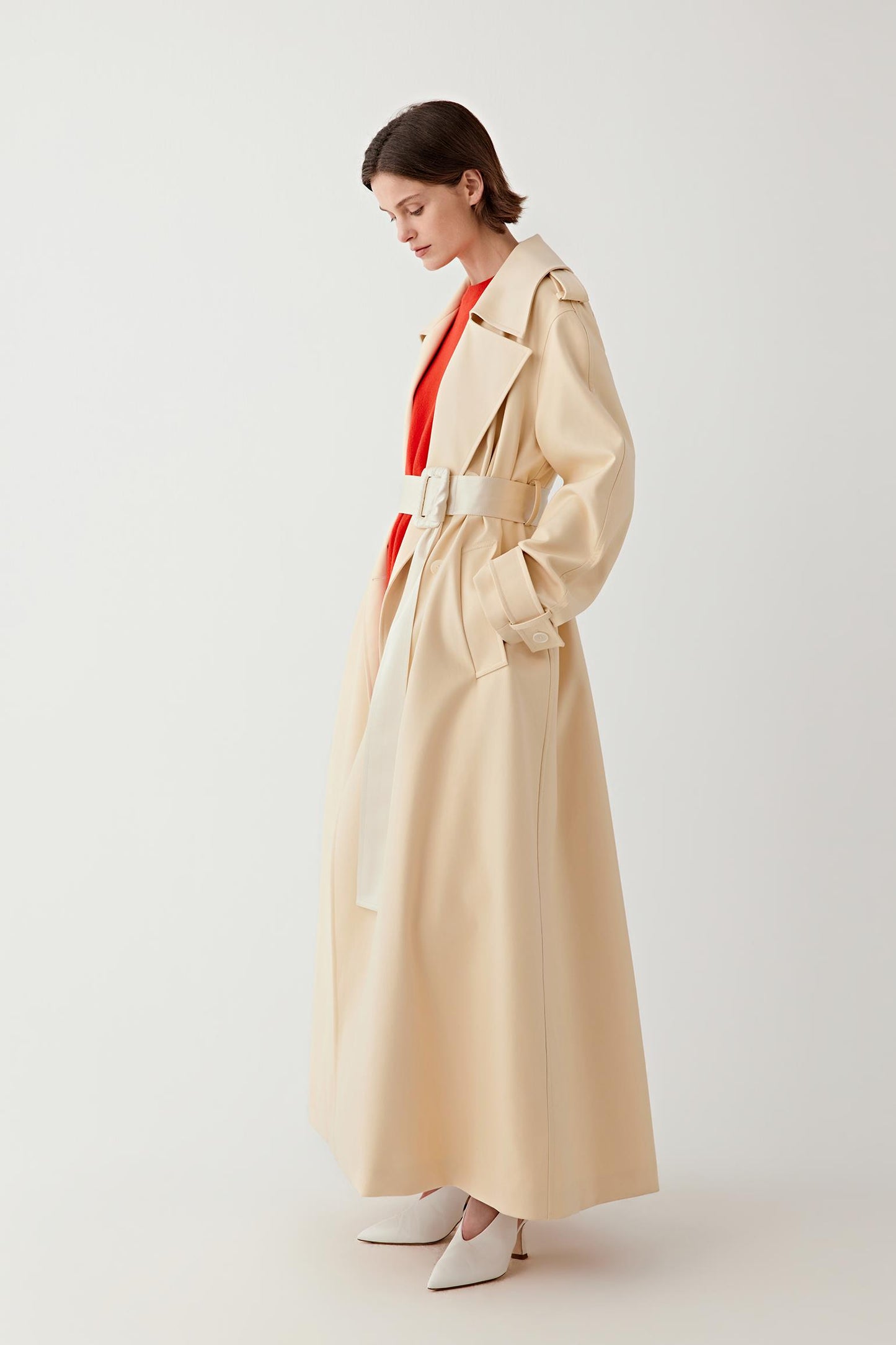 Woman wearing a beige trench coat over a red outfit on a white background