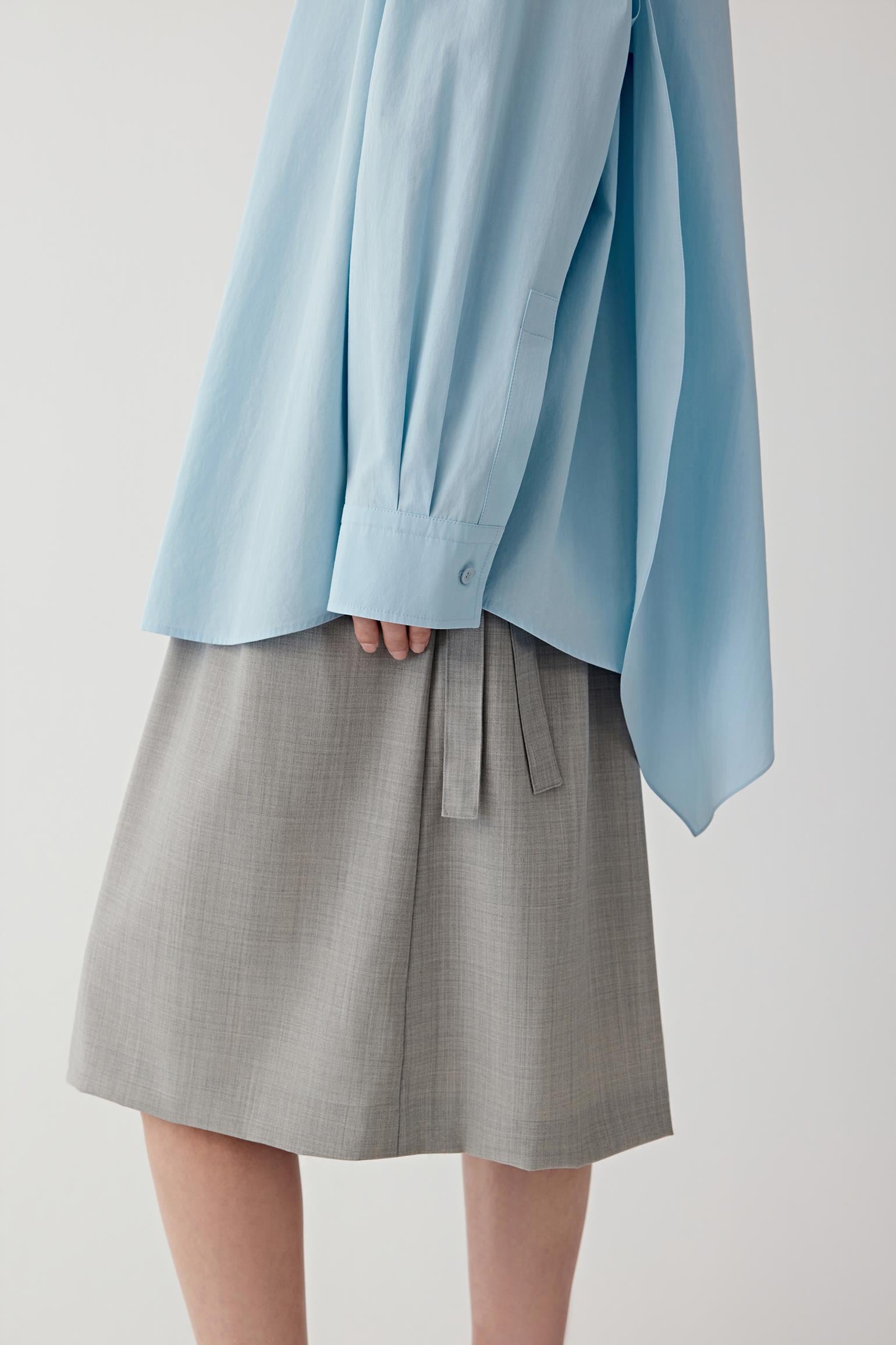 Close up of a person wearing a light blue shirt and gray short on a plain background