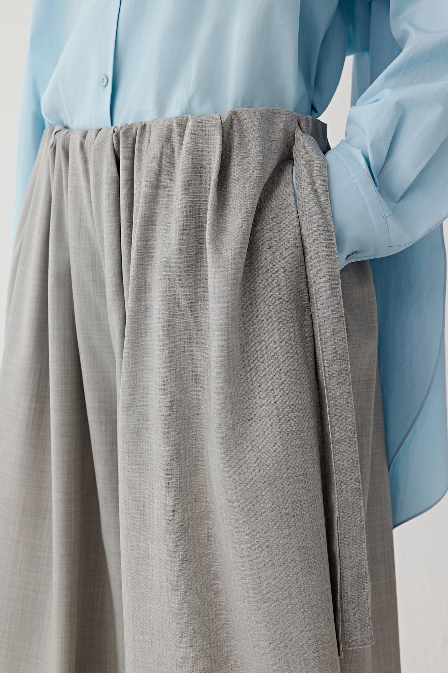 Person wearing a light blue shirt and gray pants on a plain background