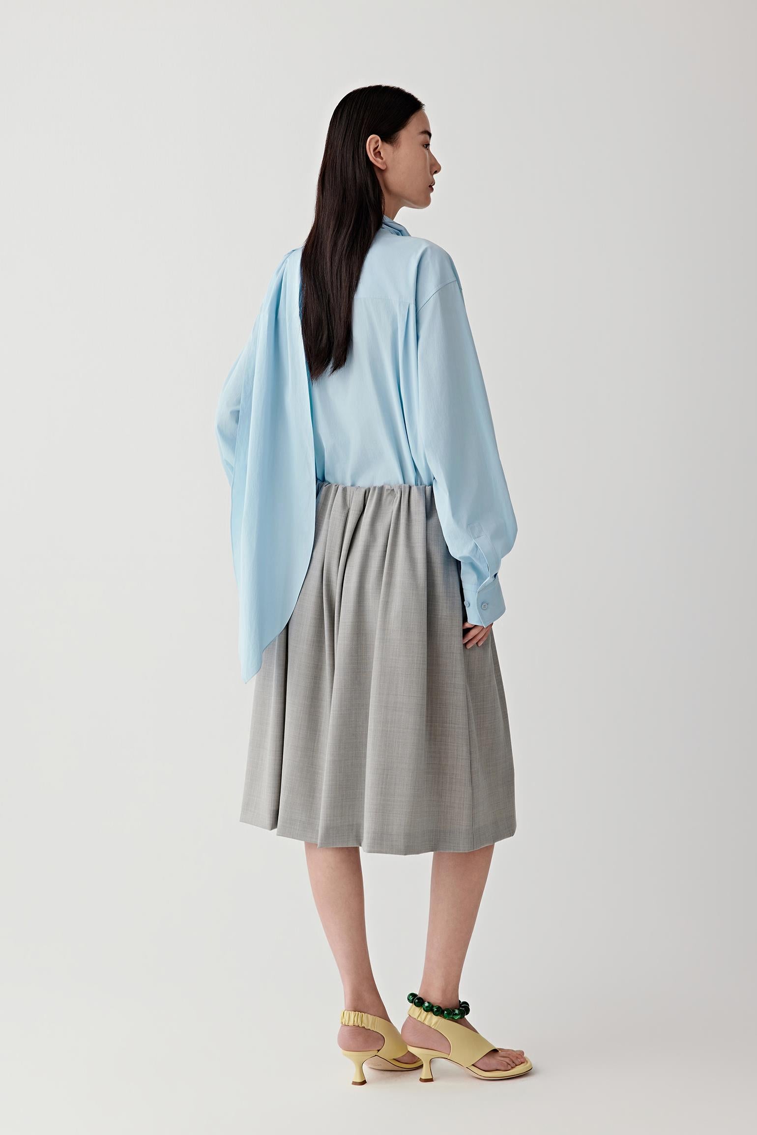 Woman wearing a light blue shirt and gray skirt on a white background