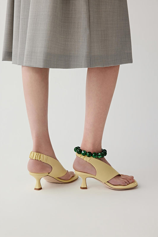 Mid-length side view of both feet, highlighting the curved mid heel, the slingback strap with gathered detail at the back of the ankle and the balanced proportion between sole and heel