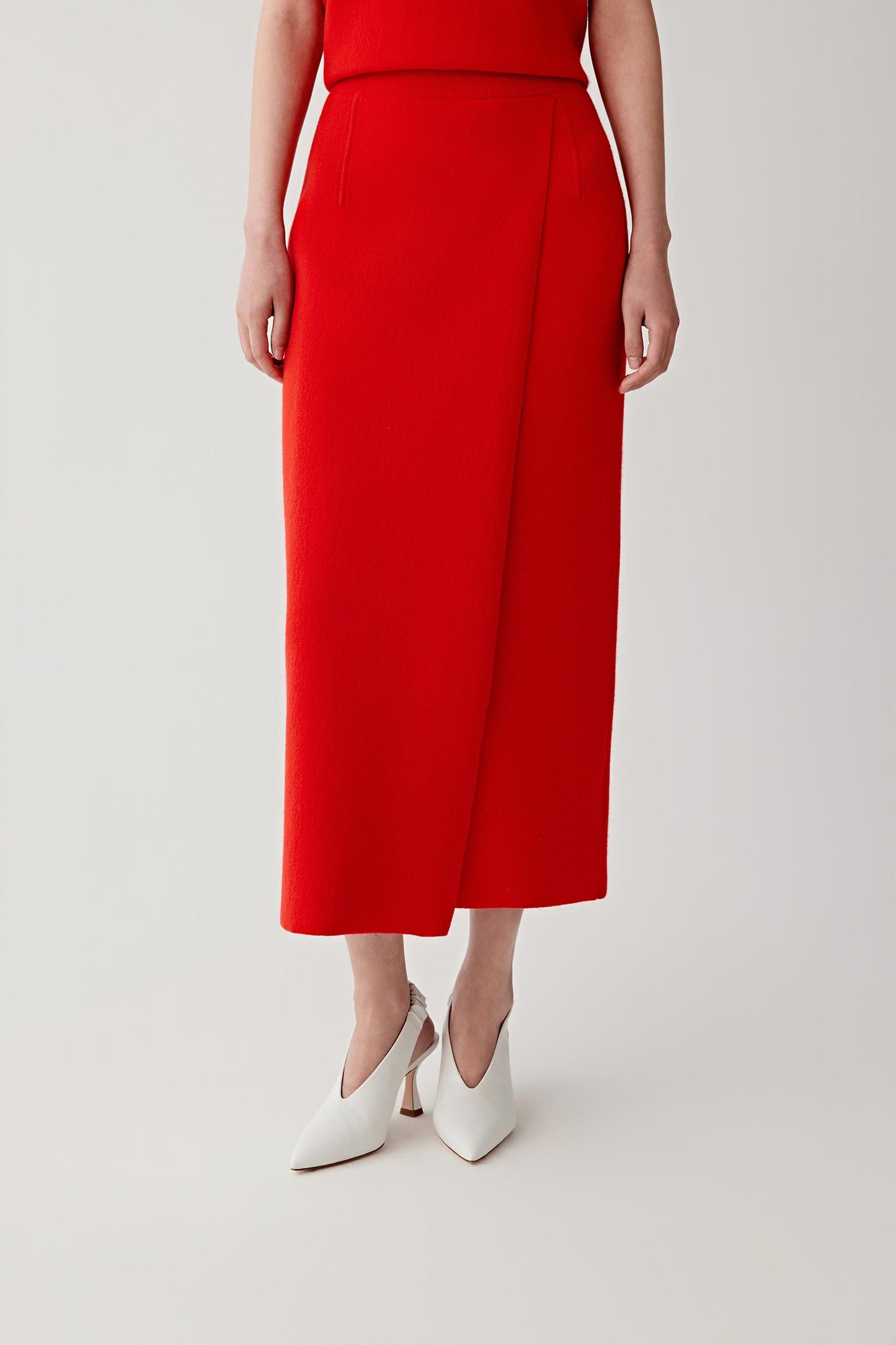 Person wearing a red skirt with white shoes on a plain background