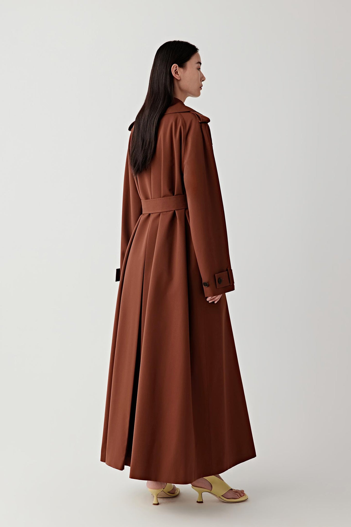 Woman wearing a long brown coat on a white background