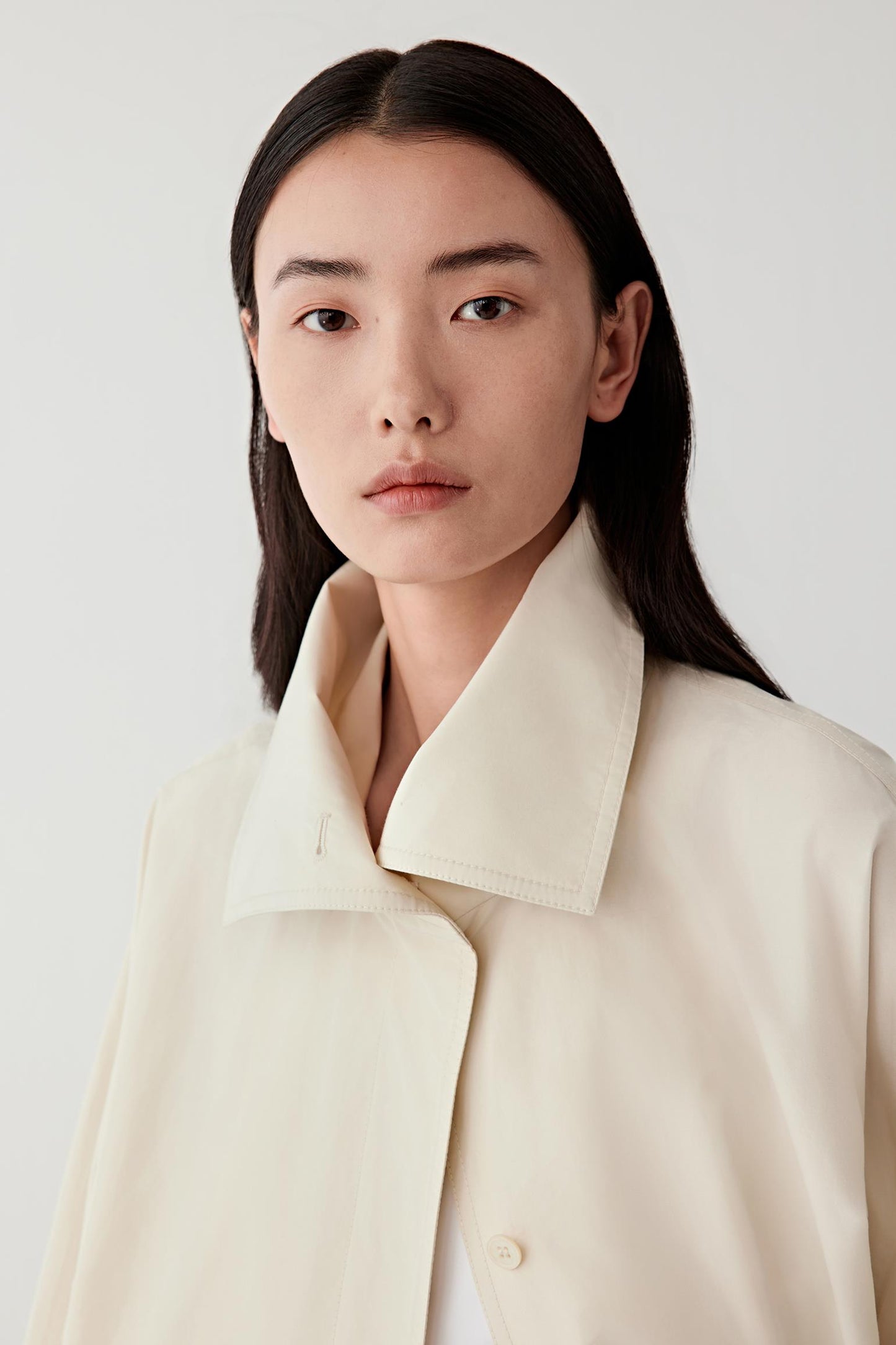Person wearing a beige coat against a white background