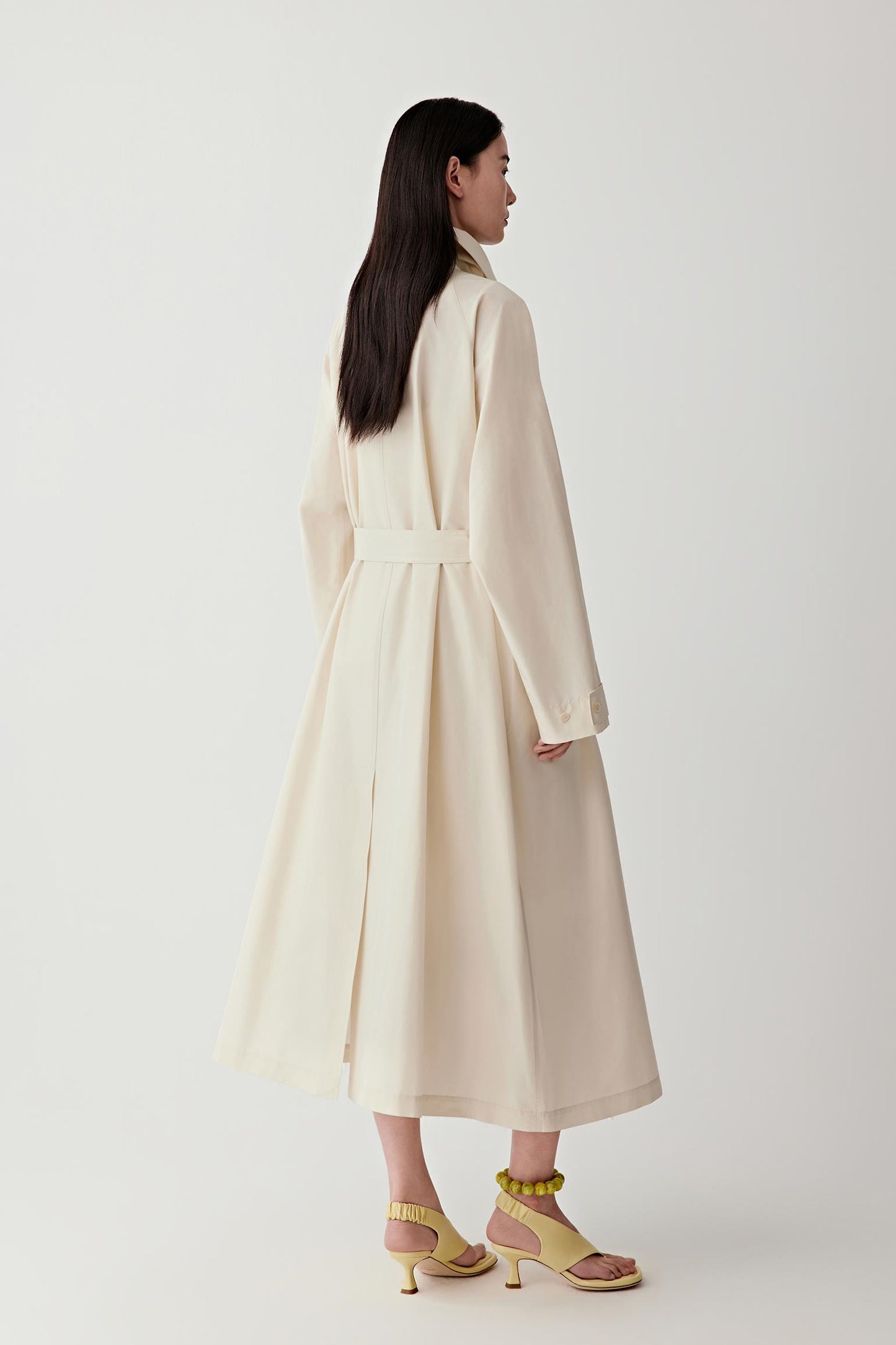 Woman wearing a long beige coat on a white background